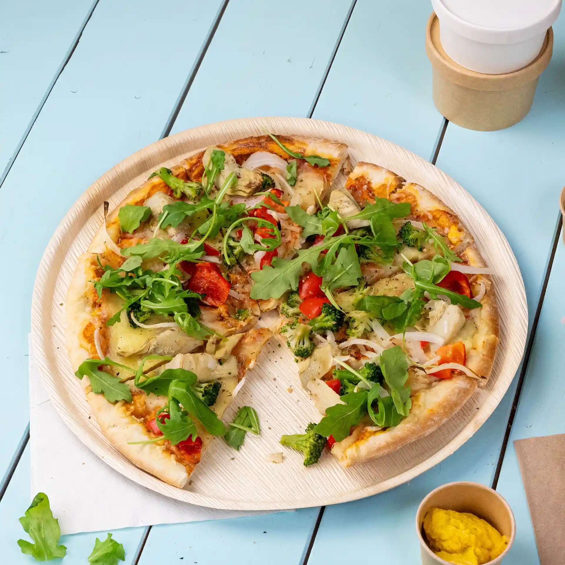 Round palm leaf pizza plate with a diameter of 27 cm, holding a sliced pizza topped with vegetables and arugula.