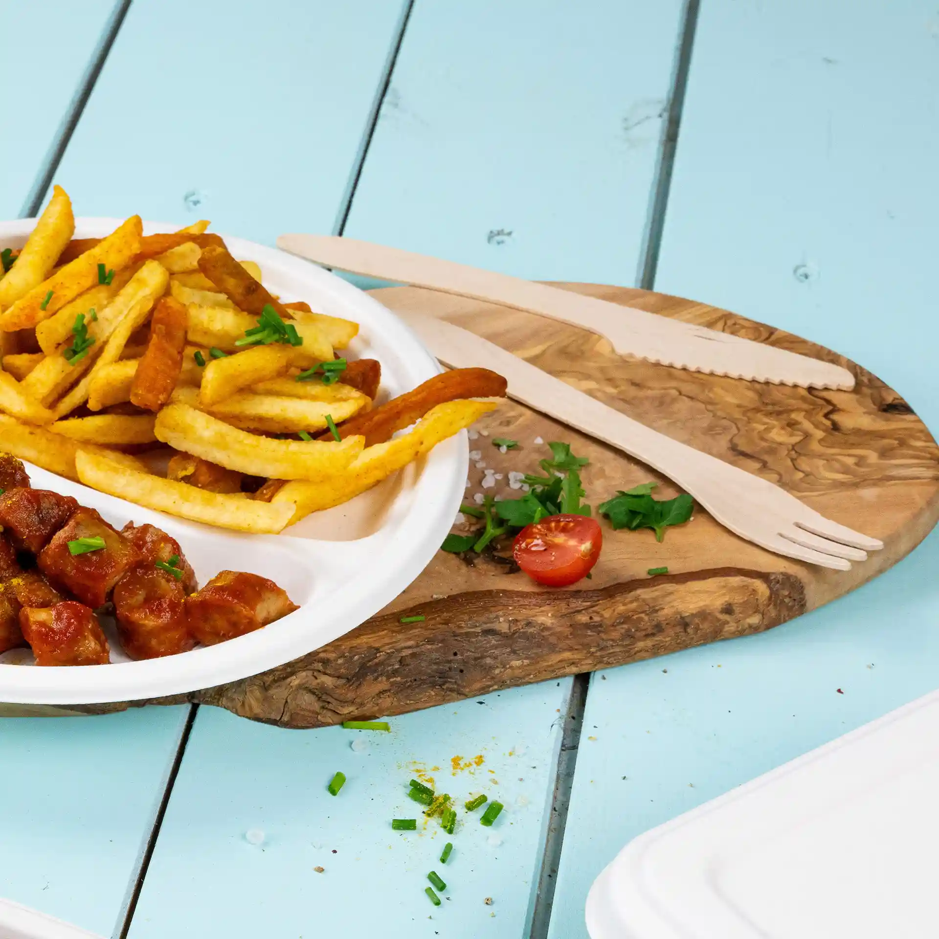 Image of a plate with French fries and sausage, accompanied by a wooden knife and fork on a wooden board.