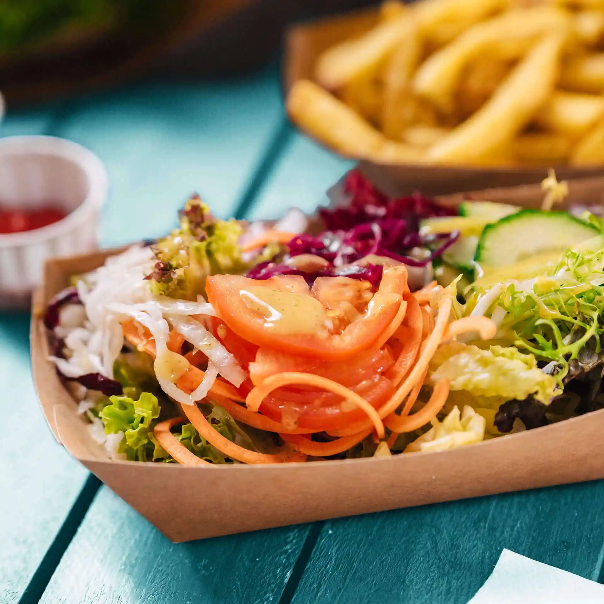 Deep rectangular cardboard snack bowl filled with mixed salad, including lettuce, tomatoes, and carrots.