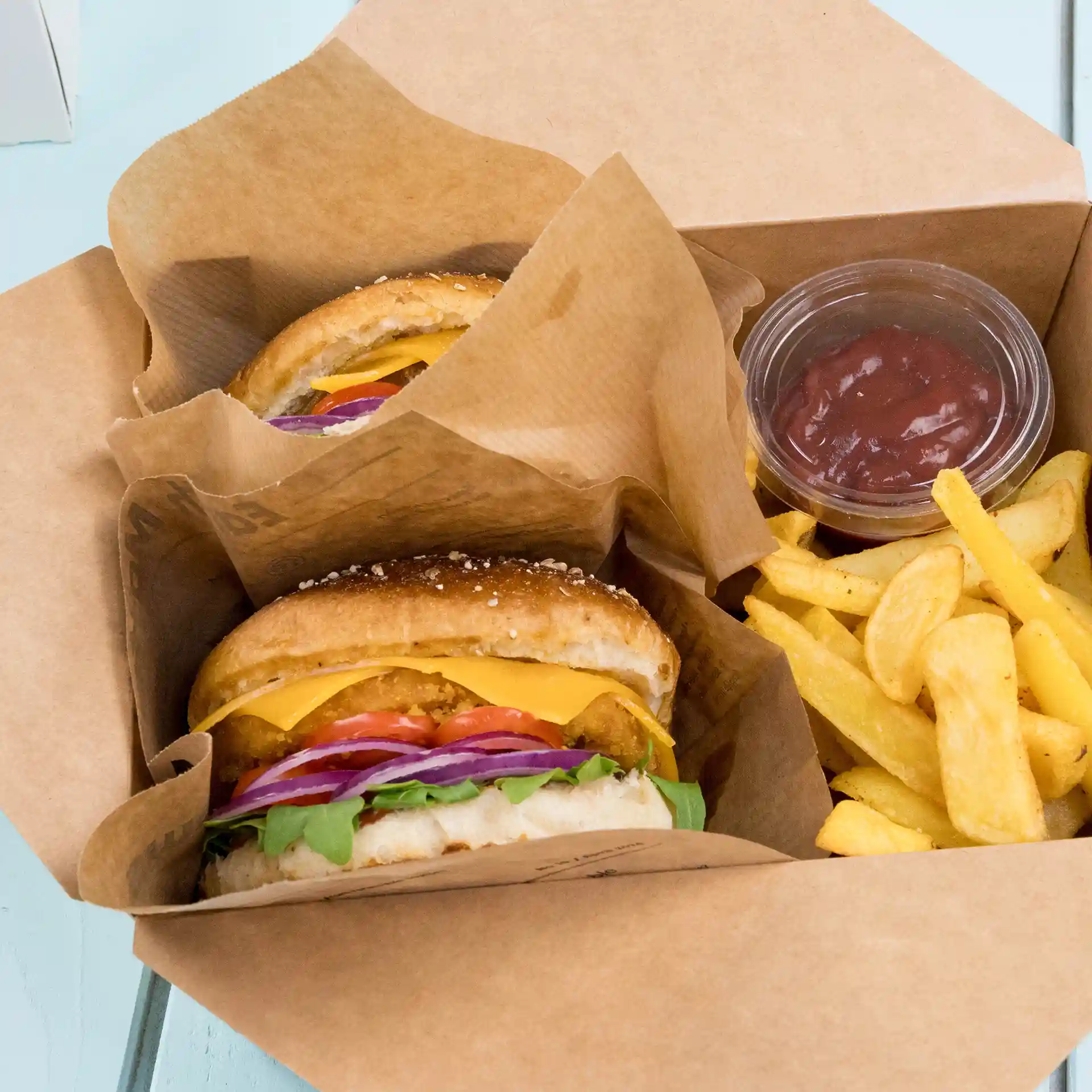 Two burgers in paper bags with a side of fries and a small container of ketchup.
