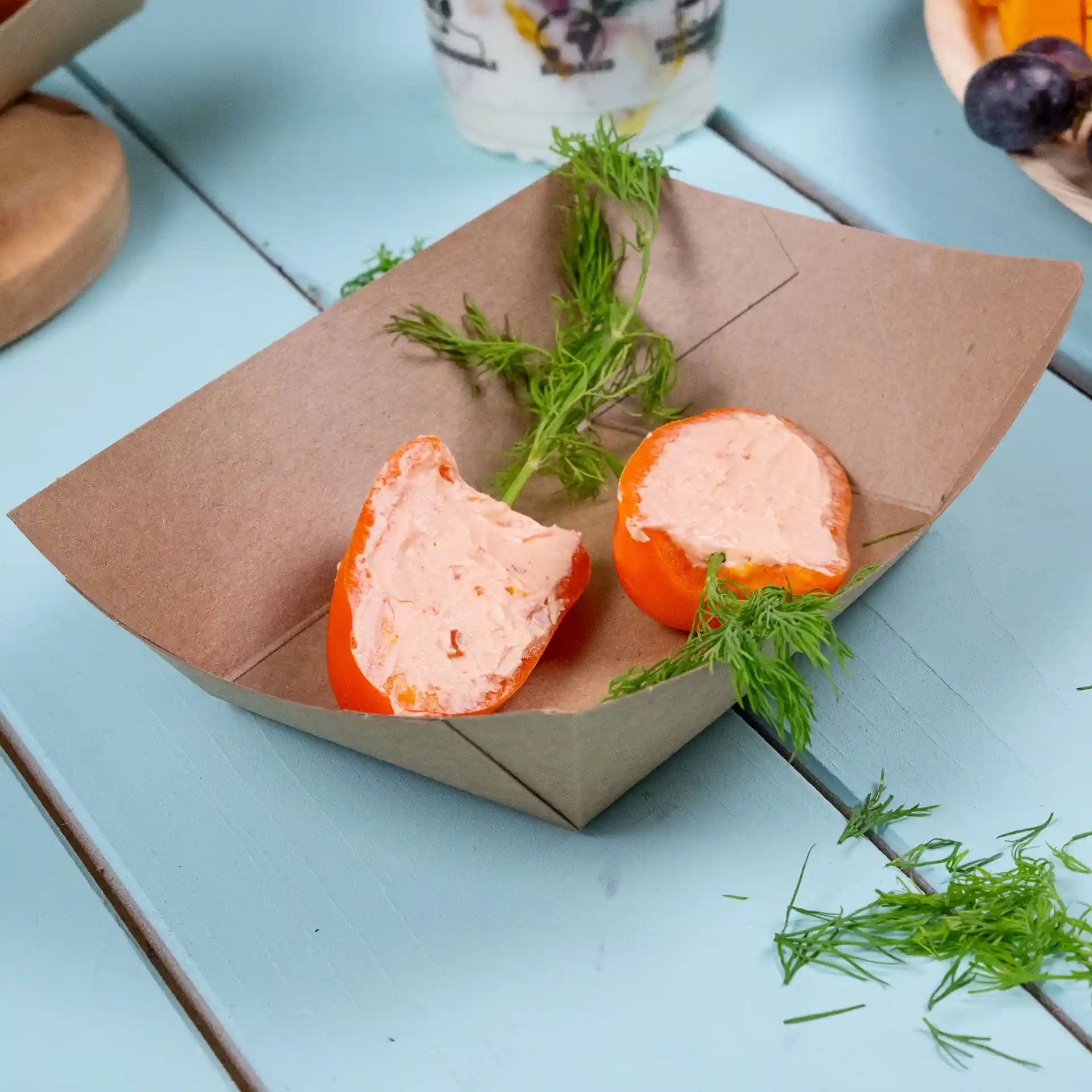 Brown cardboard food tray with two orange halves filled with a creamy substance and garnished with green herbs.