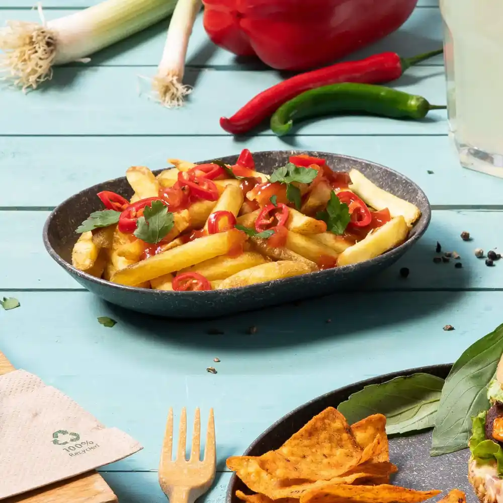 Schüssel mit Pommes frites, garniert mit in Scheiben geschnittenen Chili und Koriander auf einem blauen Holztisch.