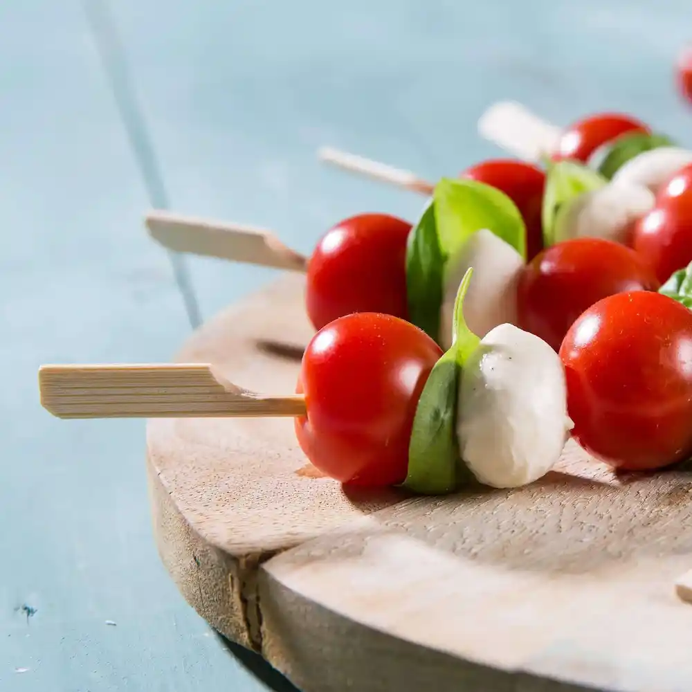Skewers with cherry tomatoes, basil leaves, and mozzarella balls arranged on a wooden serving board.