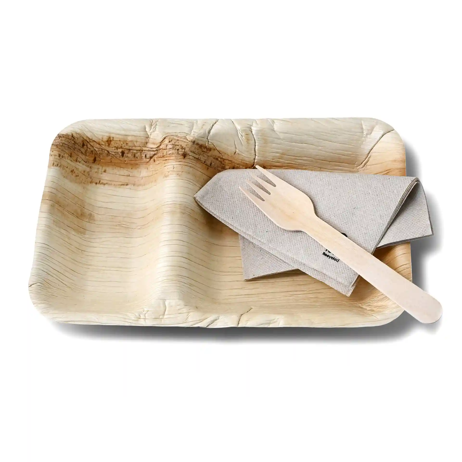 Rectangular palm leaf dinner plate with two compartments, accompanied by a beige napkin and wooden fork.
