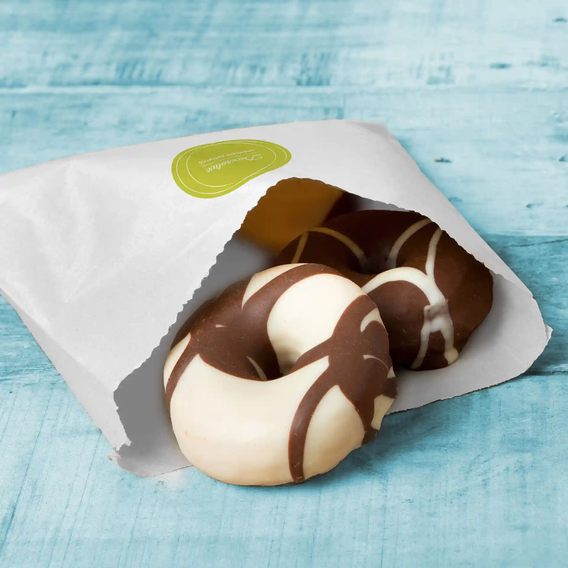 Weißer Flachbeutel teilweise geöffnet, mit zwei runden Keksen mit Schokoladen- und weißen Zuckerguss-Designs.