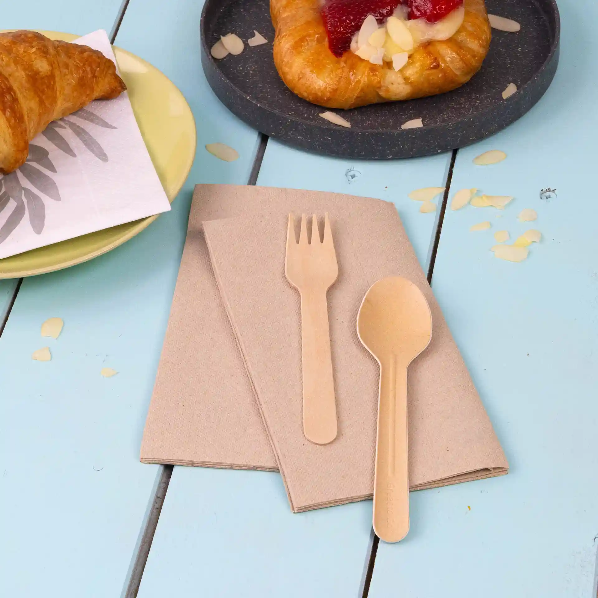 Set of unbleached recycled paper napkins with a wooden fork and spoon on a blue wooden table.