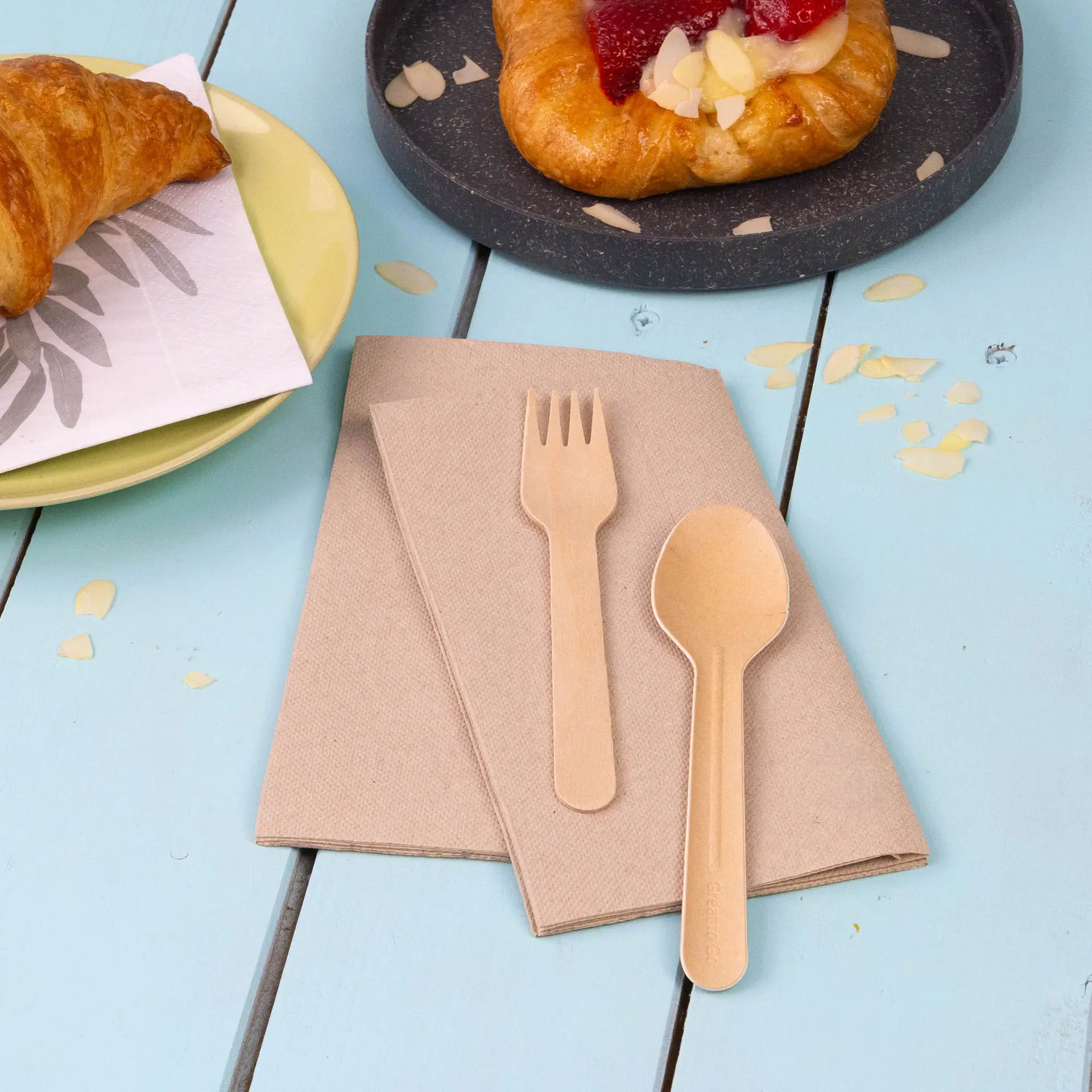 Two unbleached recycled paper napkins with a wooden fork and spoon on a blue table.