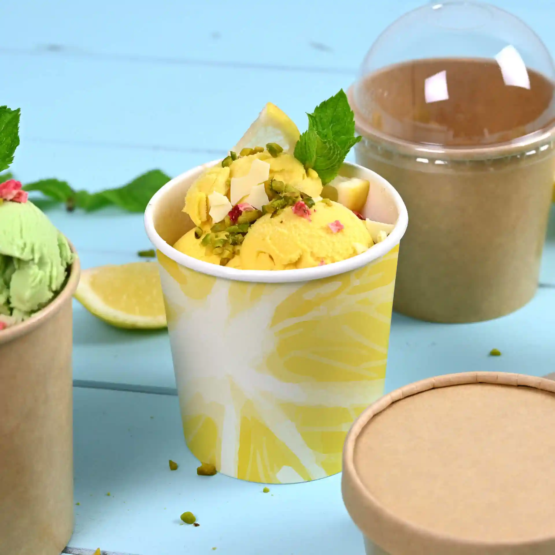 Round ice cream cup with a yellow design, filled with ice cream and garnished, on a blue background with a lid nearby.