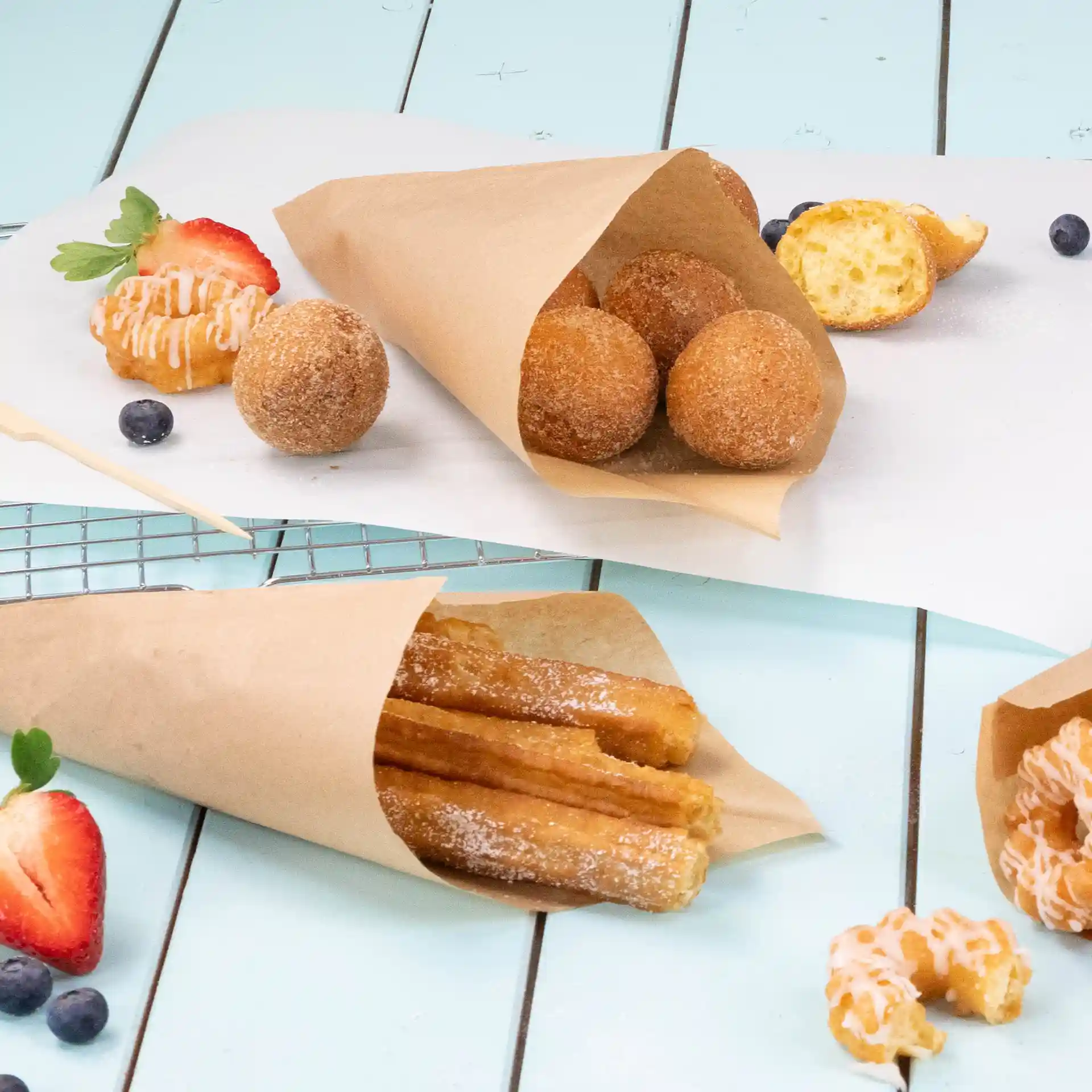Bild von braunen Papiertüten mit frittierten Snacks, darunter Churros und Donutlöcher, auf einer hellblauen Oberfläche.