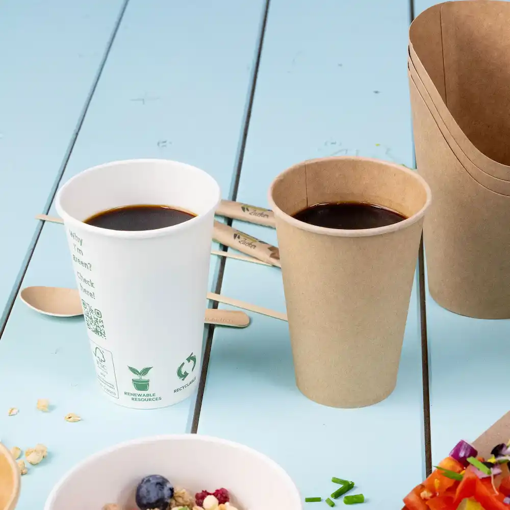 Zwei Becher mit Kaffee, einer weiß und der andere braun, neben hölzernen Rührstäben auf einer blauen Oberfläche.