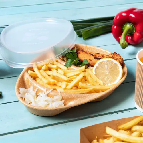 Food container with fried fish, lemon, french fries, and salad, accompanied by green onions and a red bell pepper.