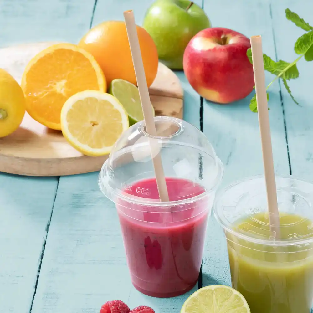 Two clear cups with colorful smoothies, one pink and one green, beside sliced citrus fruits on a wooden board.