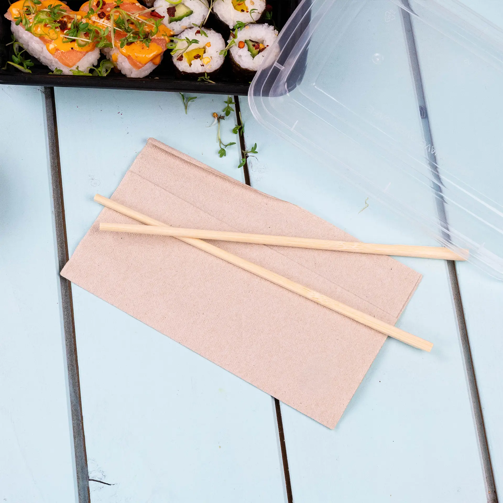 Paper napkin in unbleached color with two wooden chopsticks placed on top, on a light blue surface.