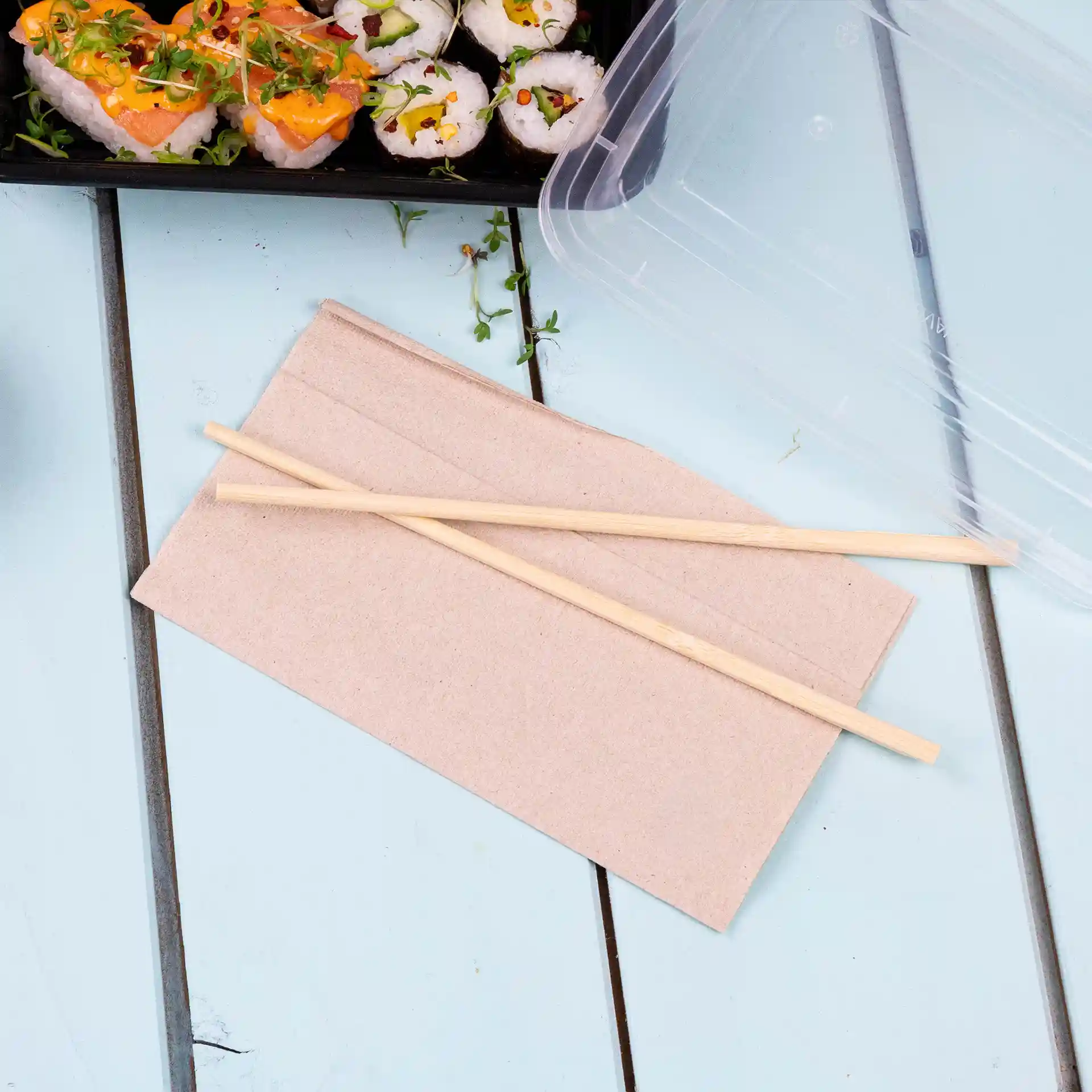 Paper napkin in unbleached color with two wooden chopsticks placed on top, on a light blue surface.
