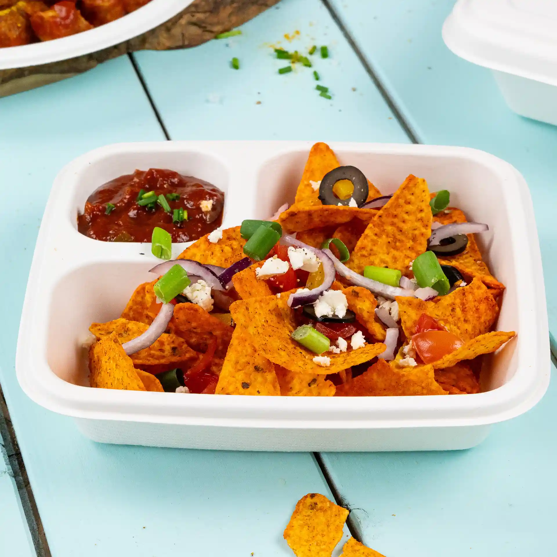 Rechteckiger weißer Zuckerrüben-Dip-Teller gefüllt mit Nachos, belegt mit Tomaten, Oliven, Zwiebeln und Frühlingszwiebeln, mit Salsa daneben.