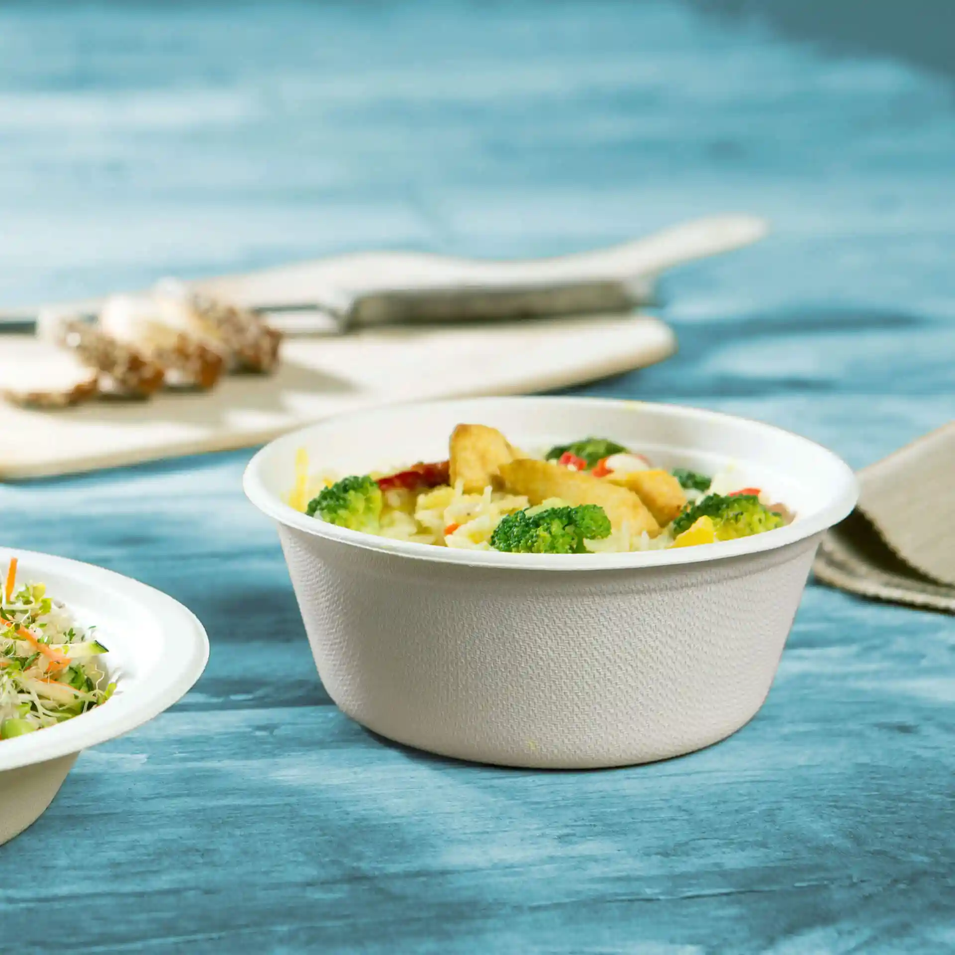 Deep round sugarcane bowl in white, holding rice and vegetables, placed on a blue wooden surface.