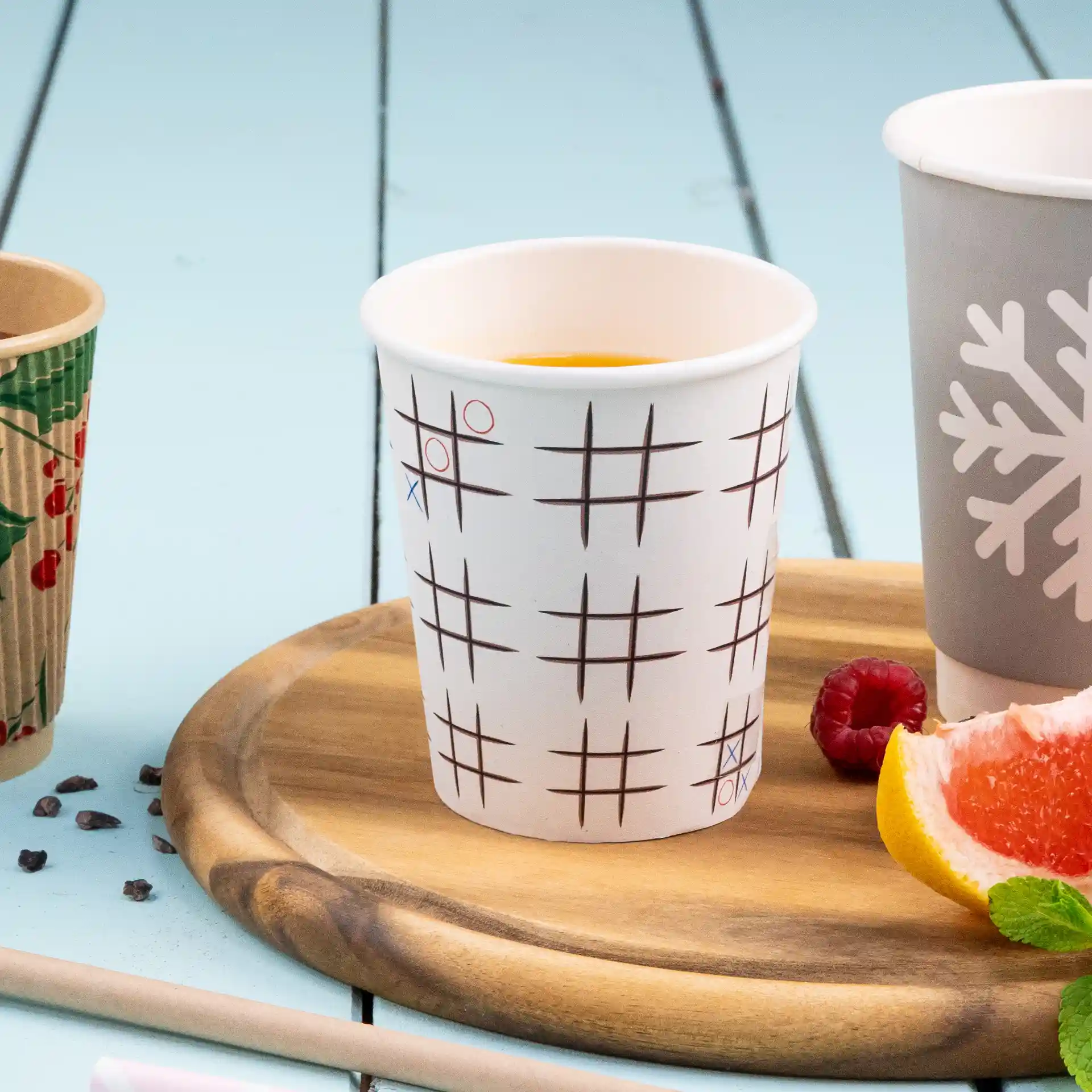 Weißer Becher mit einem Tic-Tac-Toe-Muster, auf einem Holztablett mit Obst und einem weiteren Becher daneben.