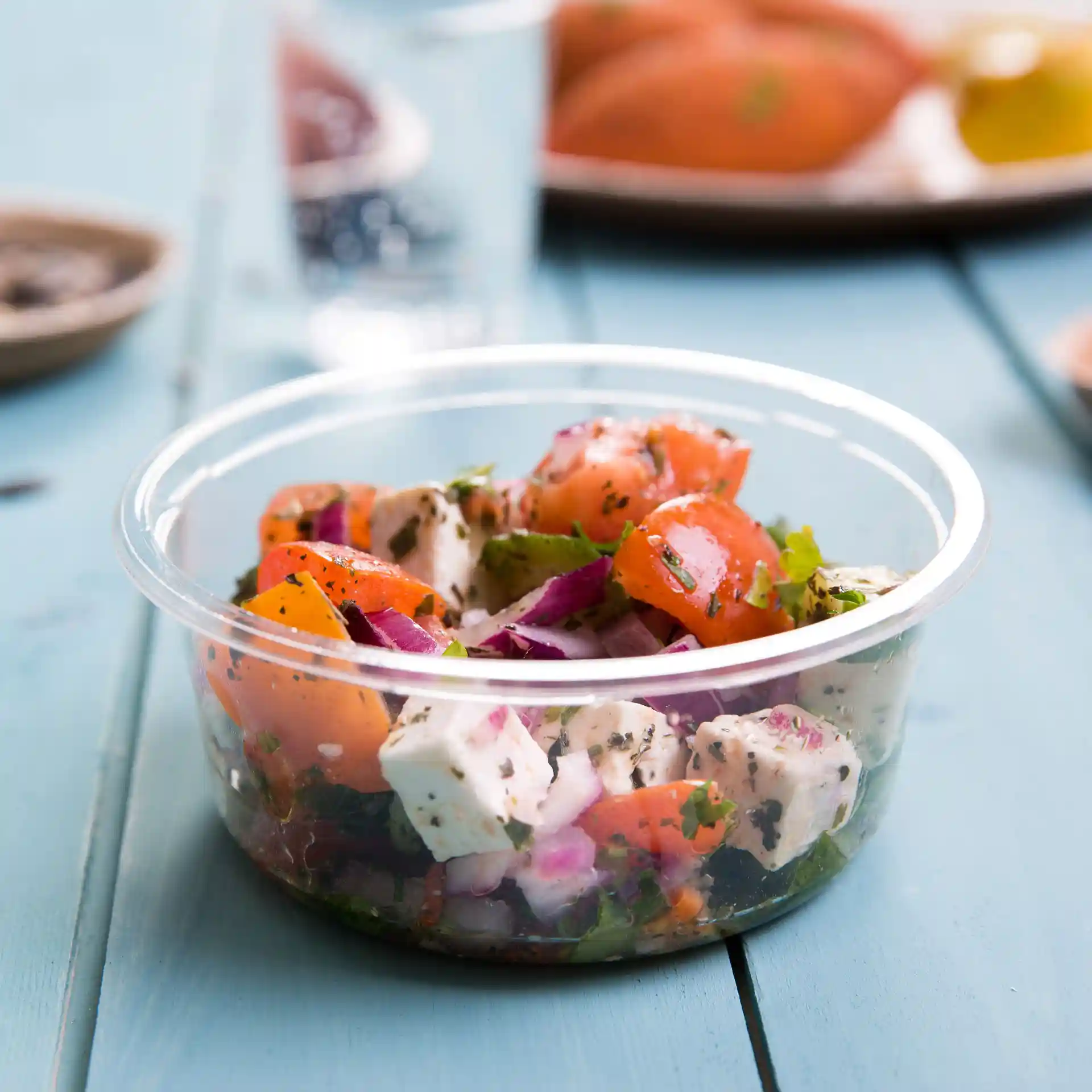 Transparenter runder Deli-Behälter gefüllt mit Salat, mit Tomaten, Zwiebeln und Kräutern.