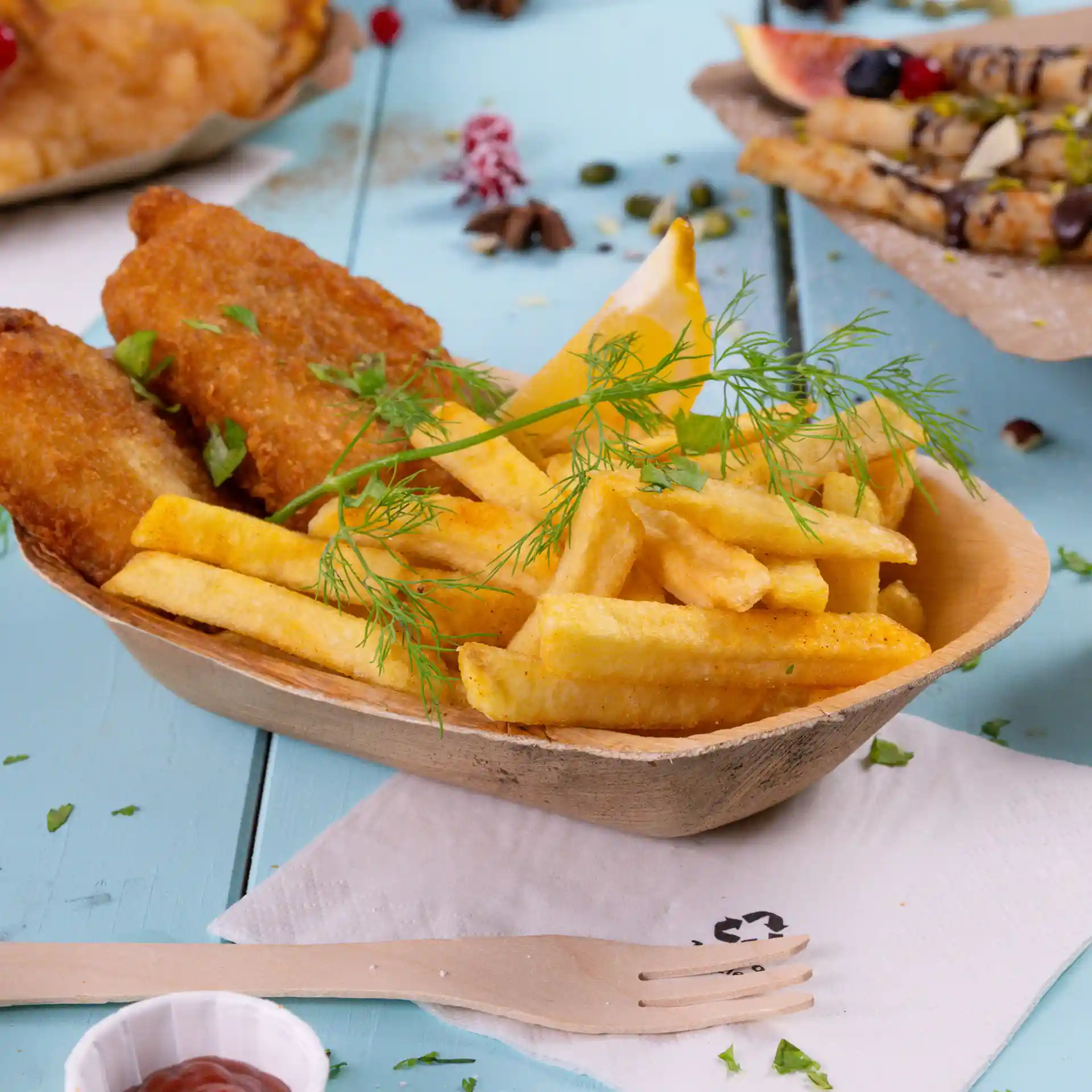 Deep palm leaf boat filled with French fries, two fried fish pieces, a lemon wedge, and a sprig of dill.