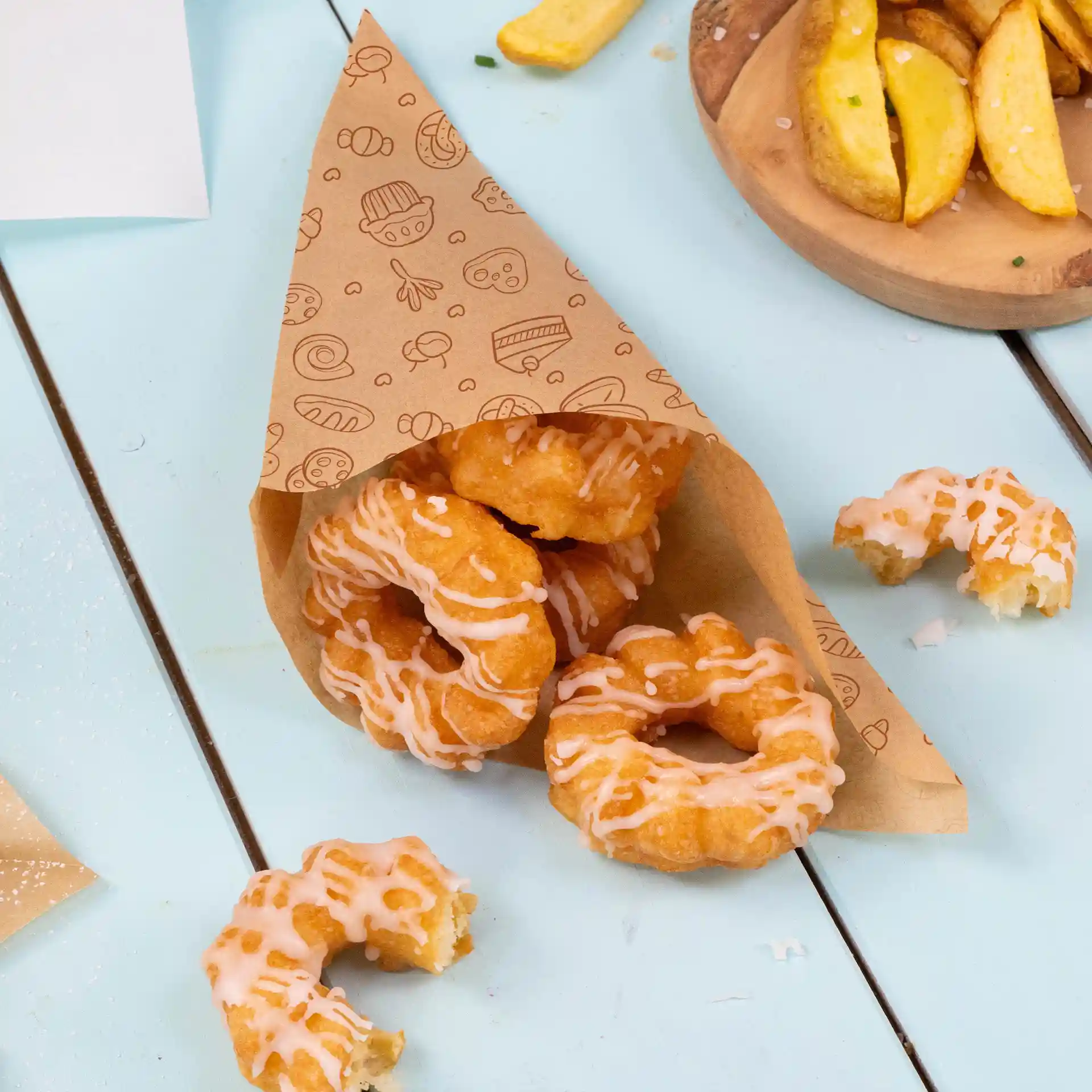 Brauner bedruckter Papierkonus gefüllt mit mehreren Eisdoughnuts auf einer hellblauen Oberfläche.