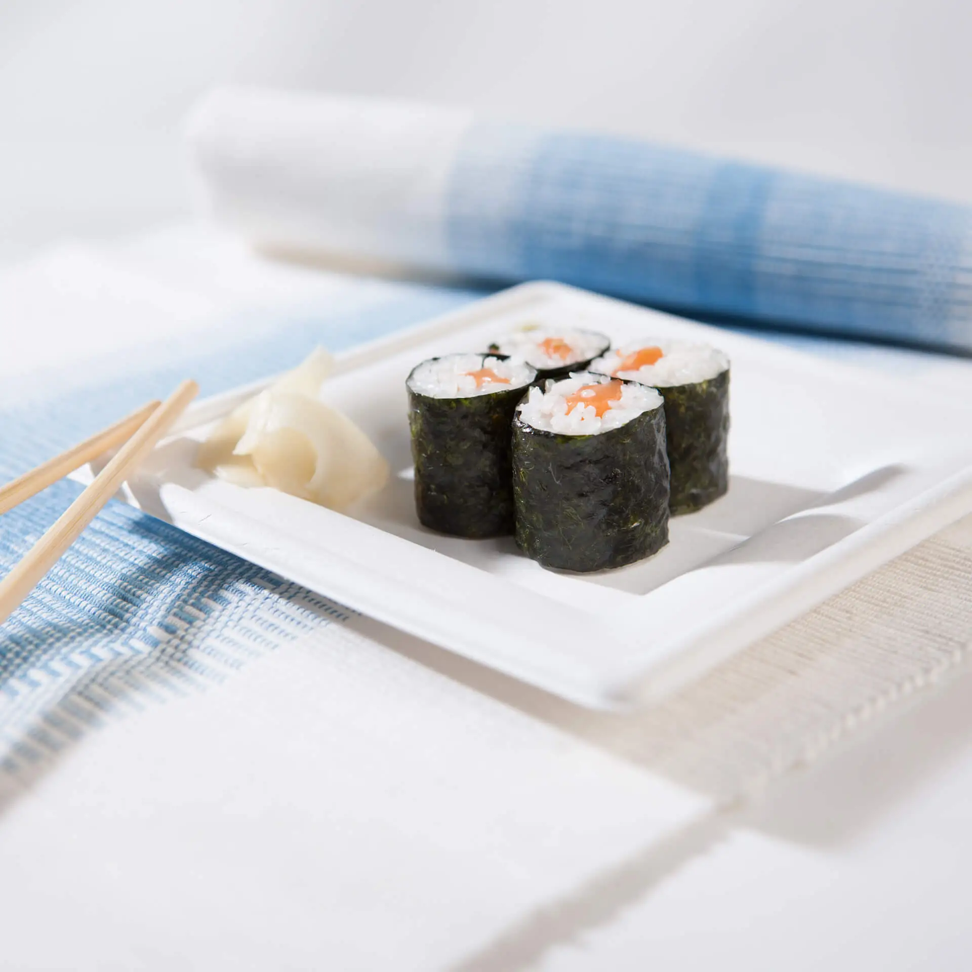 Square sugarcane plate with sushi rolls and pickled ginger, on a blue and white table setting.
