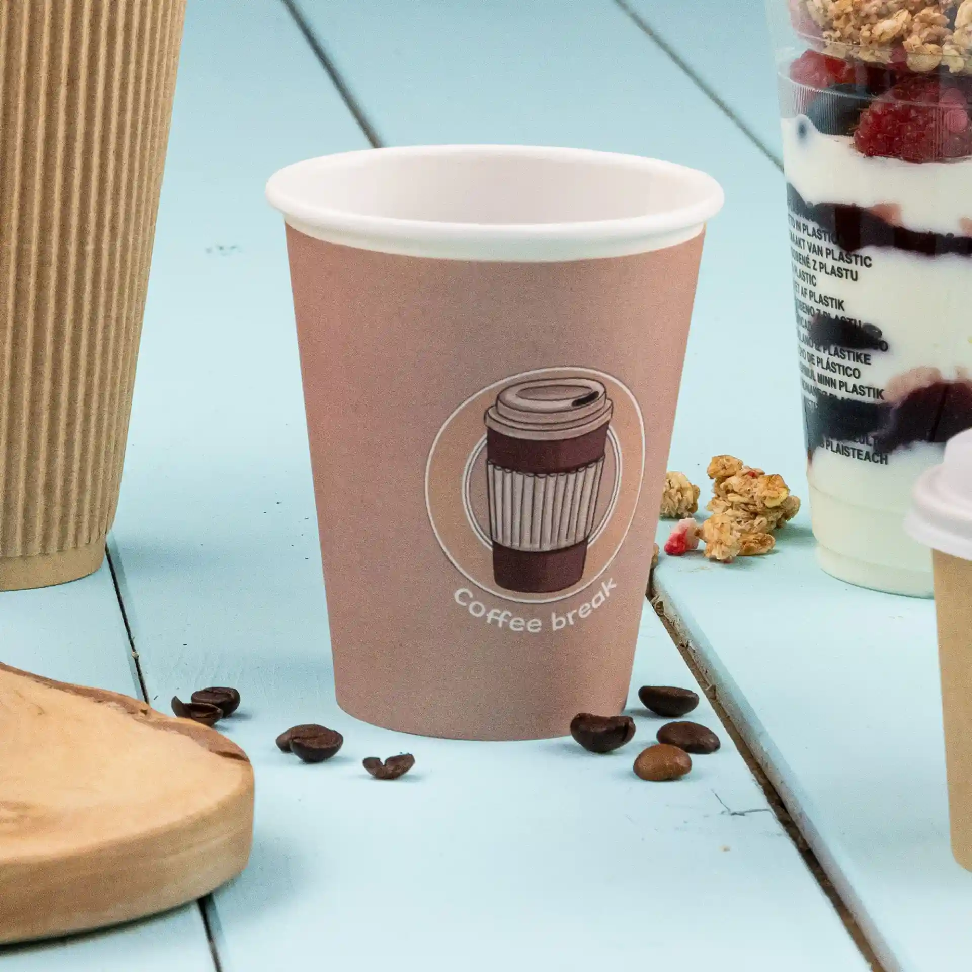 Brauner Becher aus Papier mit einem gedruckten Kaffeedesign und Text, auf einer blauen Oberfläche mit Kaffeebohnen daneben.