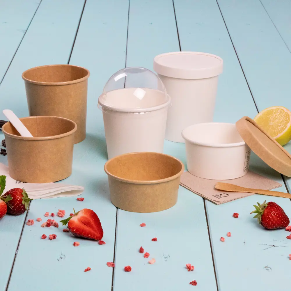 Takeaway dessert containers in various sizes, including paper and plastic, surrounded by strawberries and lemon.