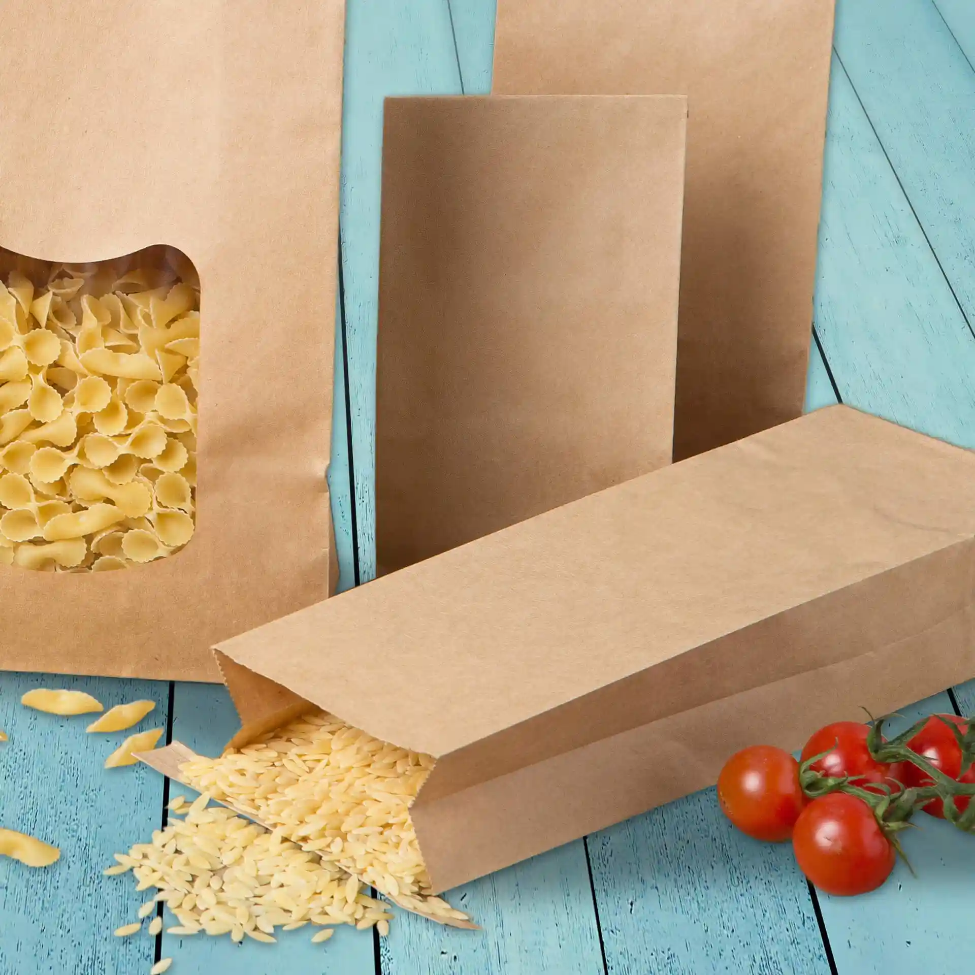 Brown kraft paper bags with pasta inside, one bag open with pasta spilling out, and cherry tomatoes nearby.