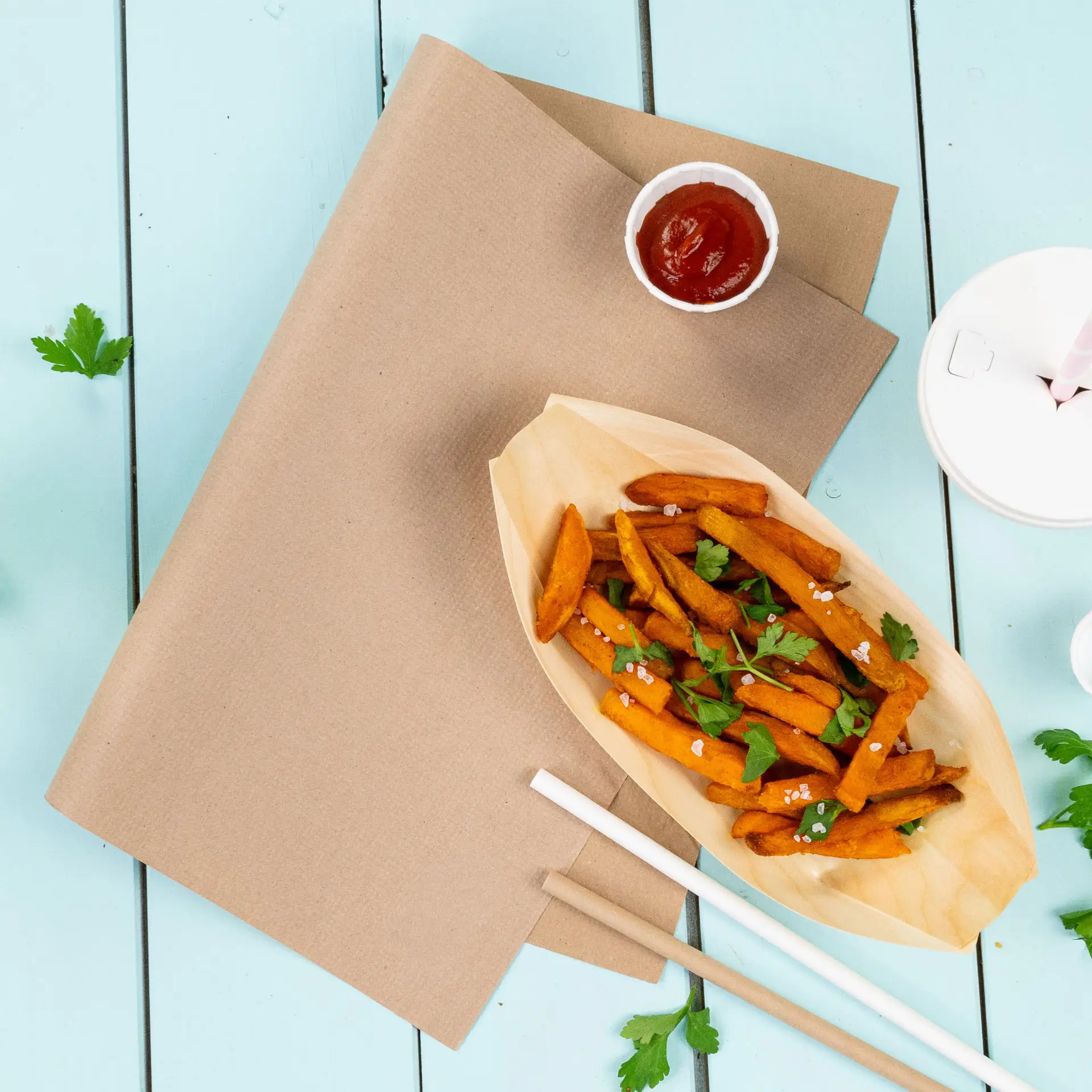 Brown rPaper placemat with sweet potato fries in a boat-shaped container, ketchup, and cilantro on a blue background.