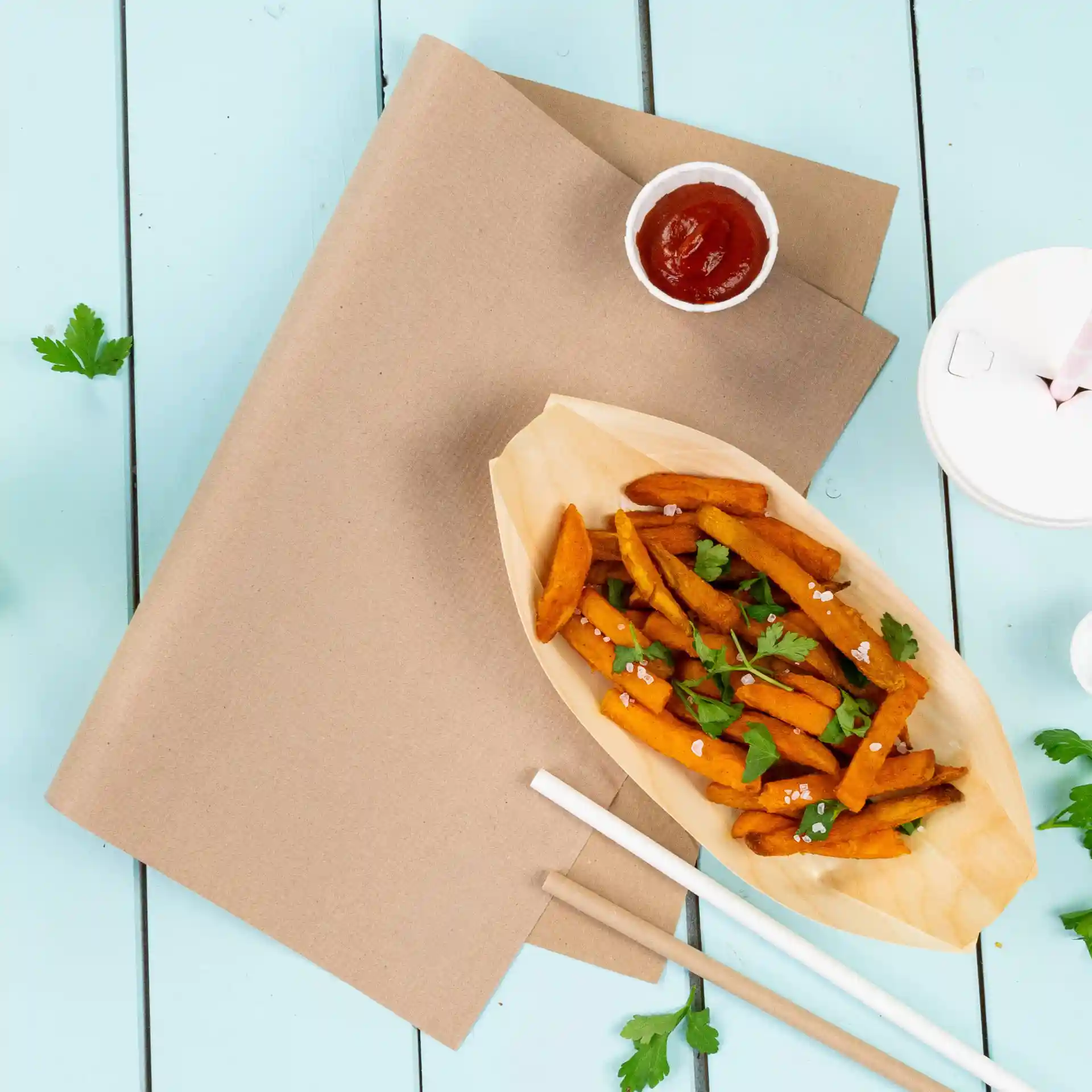 Braune Papiertischdecke mit Süßkartoffelpommes in einem bootförmigen Behälter, Ketchup und Koriander auf blauem Hintergrund.