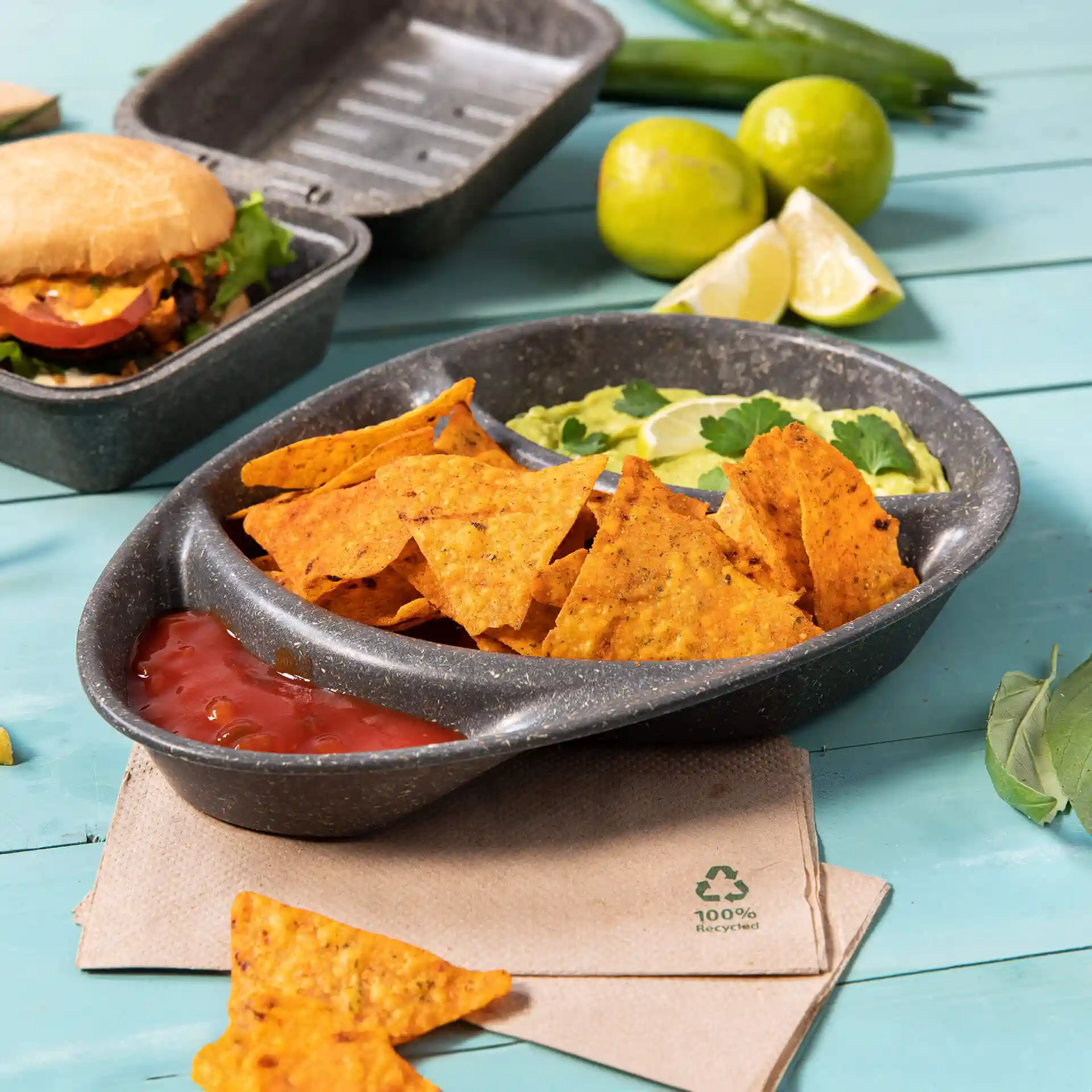Divided grey plate with three compartments, filled with tortilla chips, salsa, and guacamole, on a blue surface.