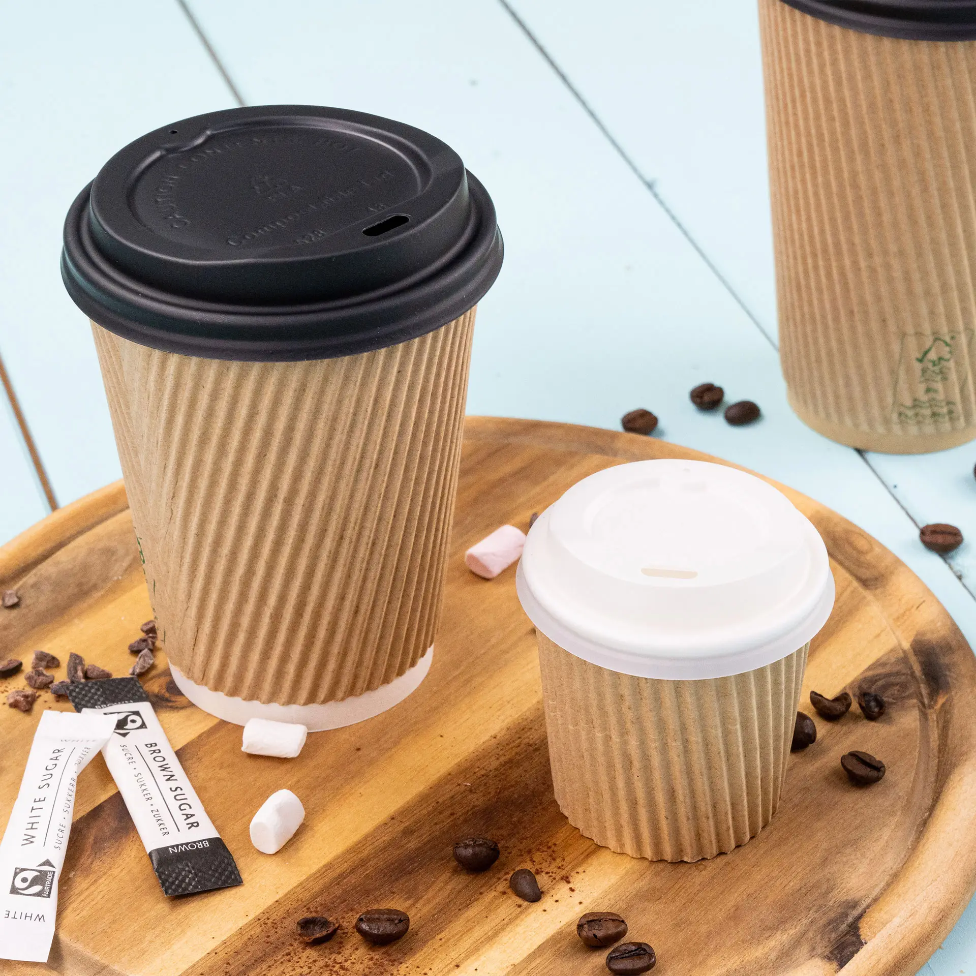 One 4 oz ribbed paper coffee cup with a black lid; another smaller cup with a white lid; coffee beans and sugar packets are nearby.