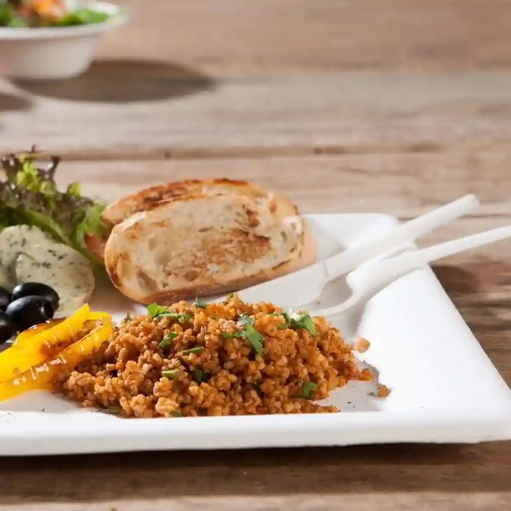 Plate with bulgur wheat, grilled vegetables, olives, a slice of bread, and a salad on a wooden table.