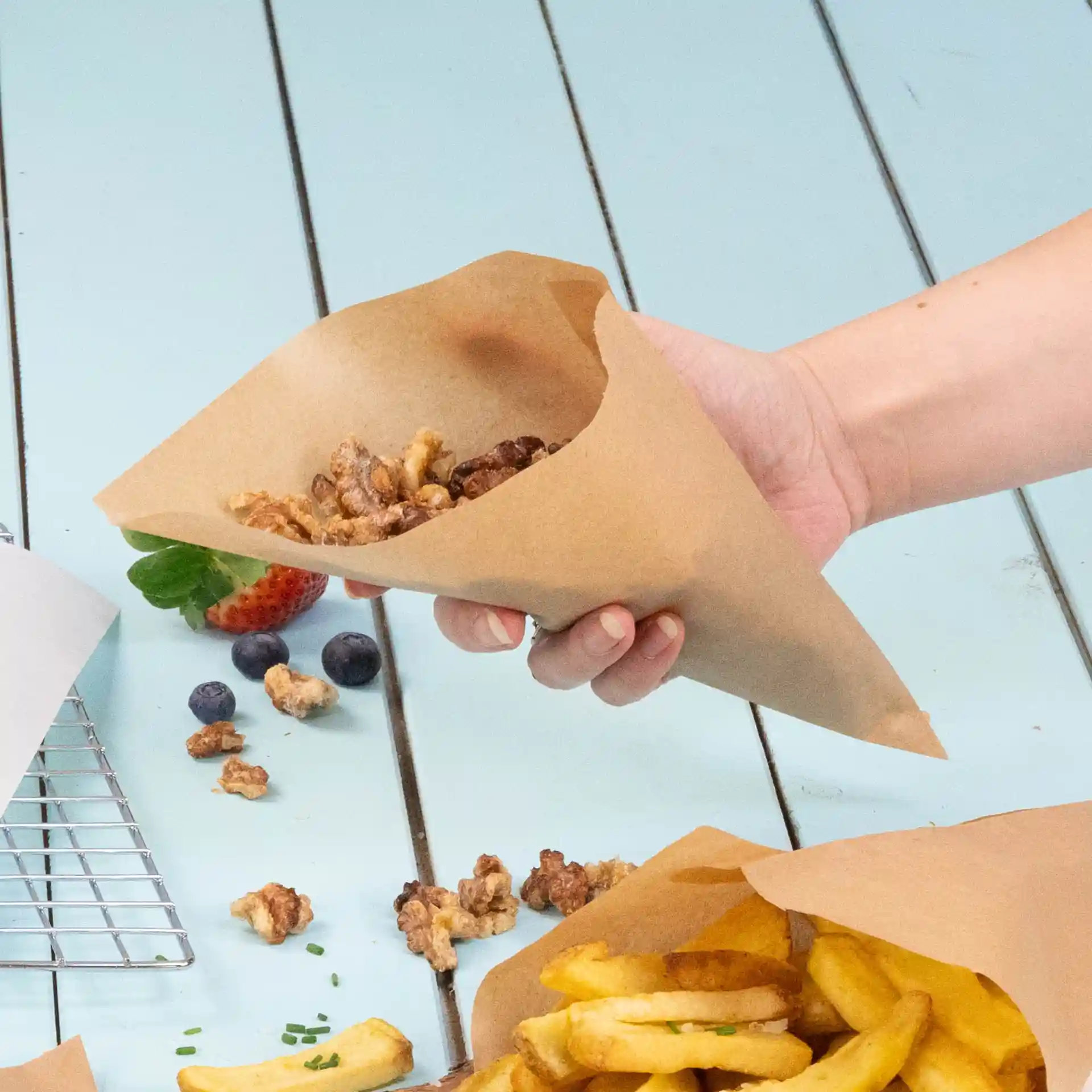 Brown paper cone holding snack food, with French fries and berries visible on a blue surface.