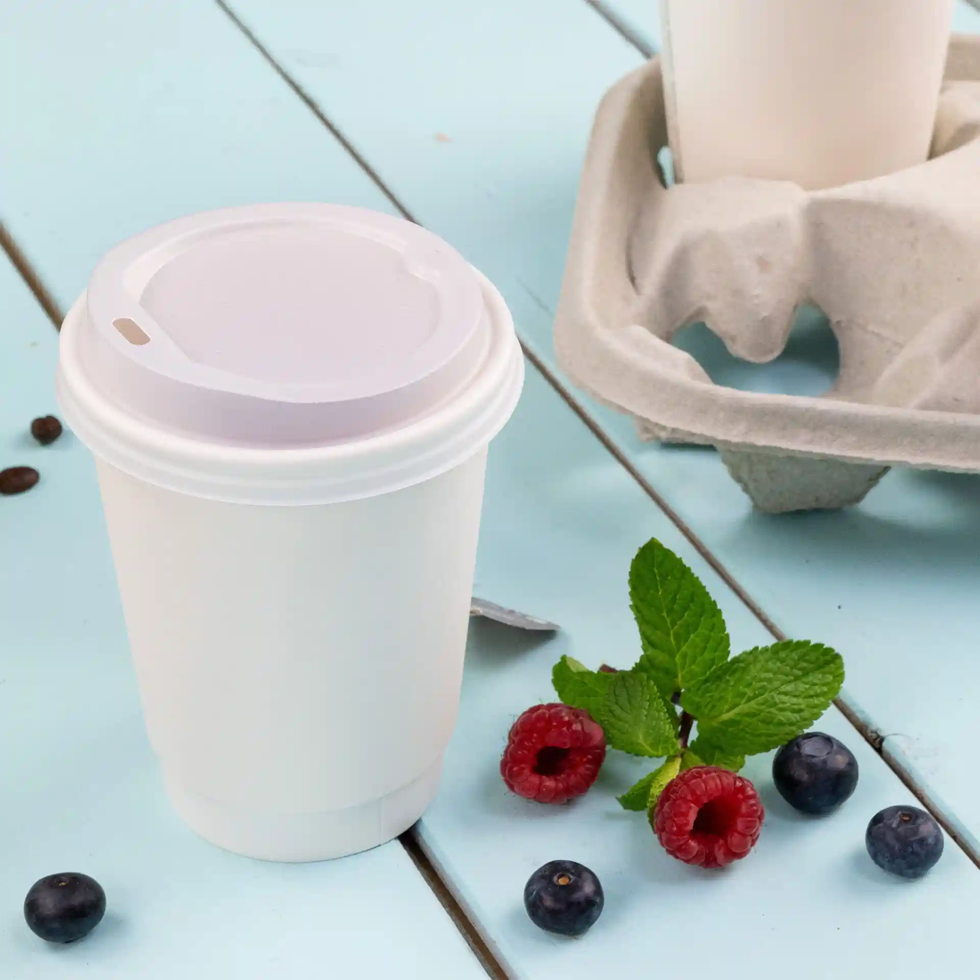 Weißer doppelwandiger Becher mit Deckel, 300 ml, auf einer blauen Oberfläche mit Himbeeren, Blaubeeren und Minzblättern.