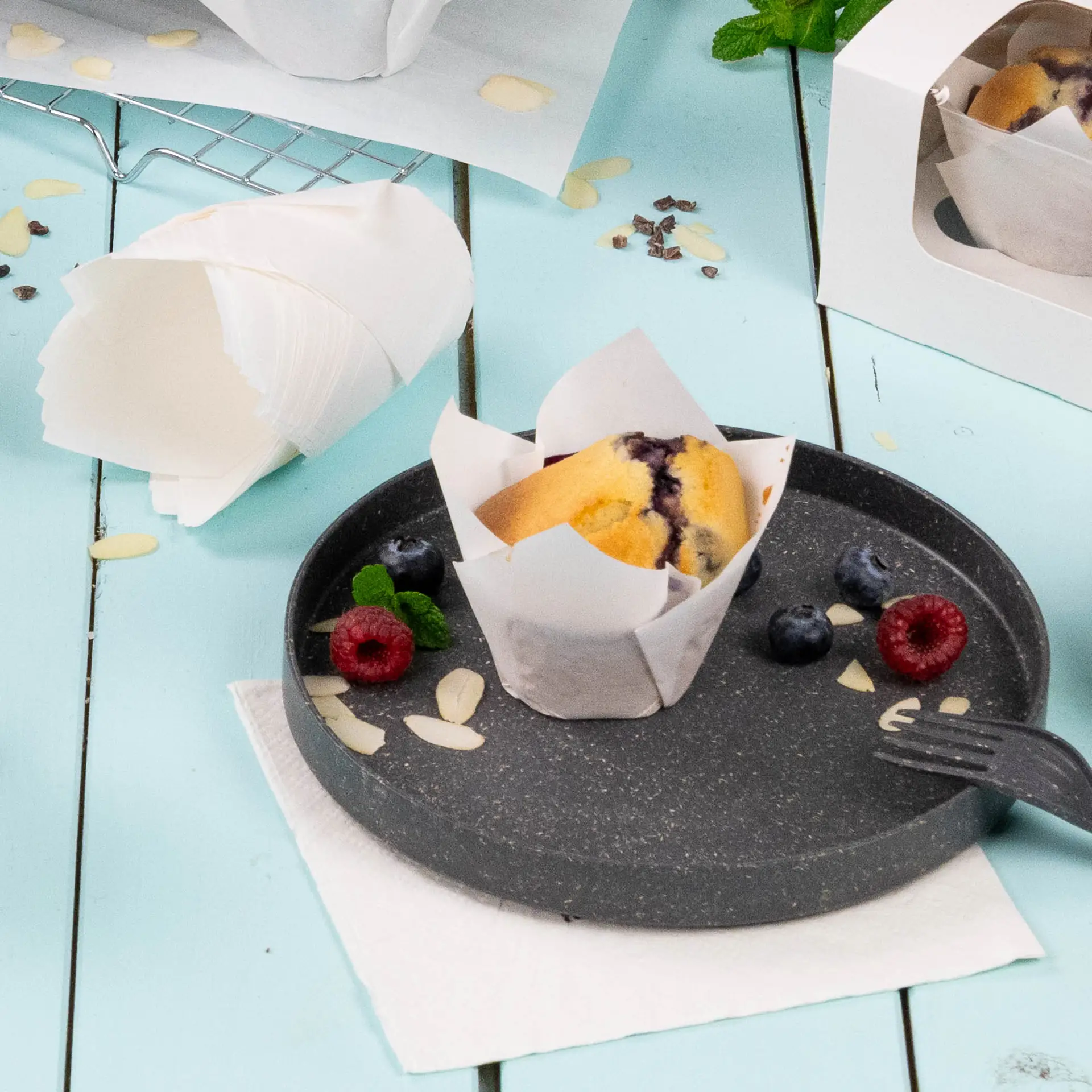 Eine weiße Muffinförmchen aus fettem Papier auf einem dunklen Teller; garniert mit Himbeeren, Heidelbeeren und Mandelblättchen.