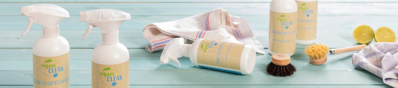 Zwei Sprühflaschen mit Reinigungsmittel, einem Tuch, einer Bürste und halbierten Limetten auf einer blauen Holzoberfläche.