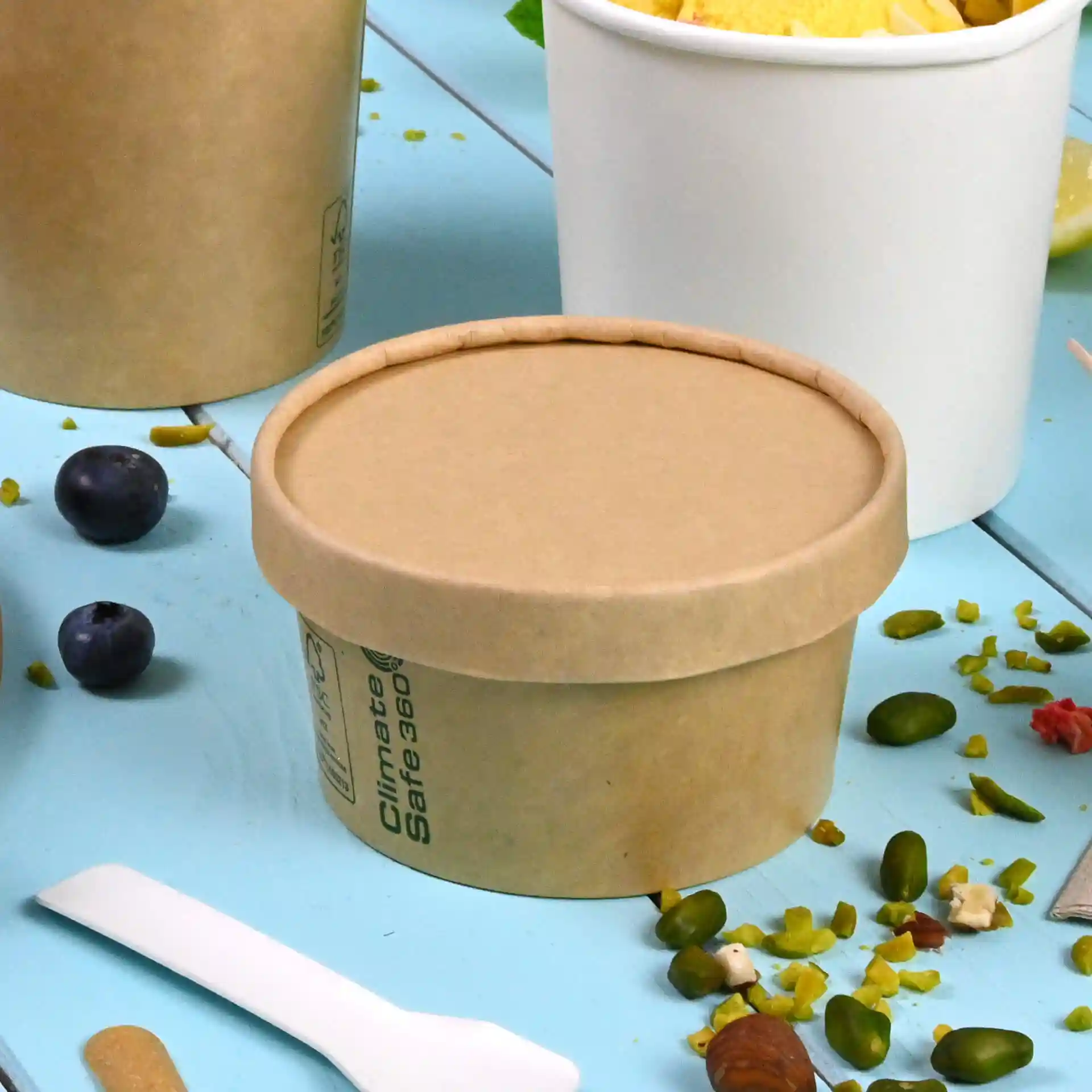 Brauner Kartondeckel in runder Form, entworfen für Becher, auf einer blauen Fläche mit verstreuten Lebensmitteln.