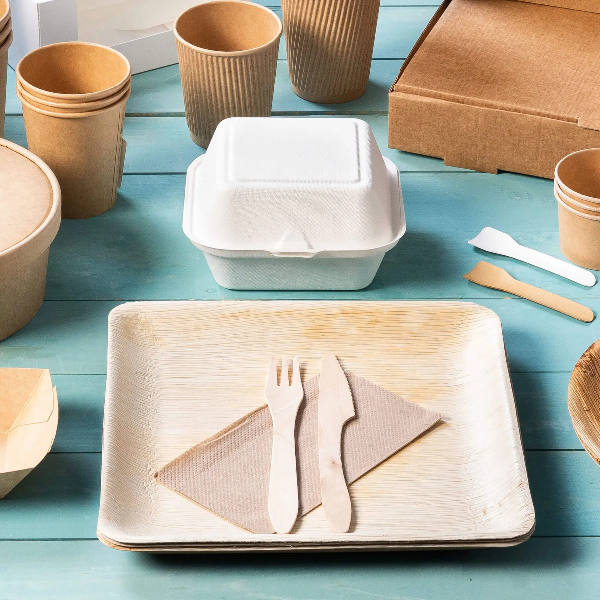 Image of various disposable food containers and utensils, including a white takeout box, wooden fork and knife on a plate.