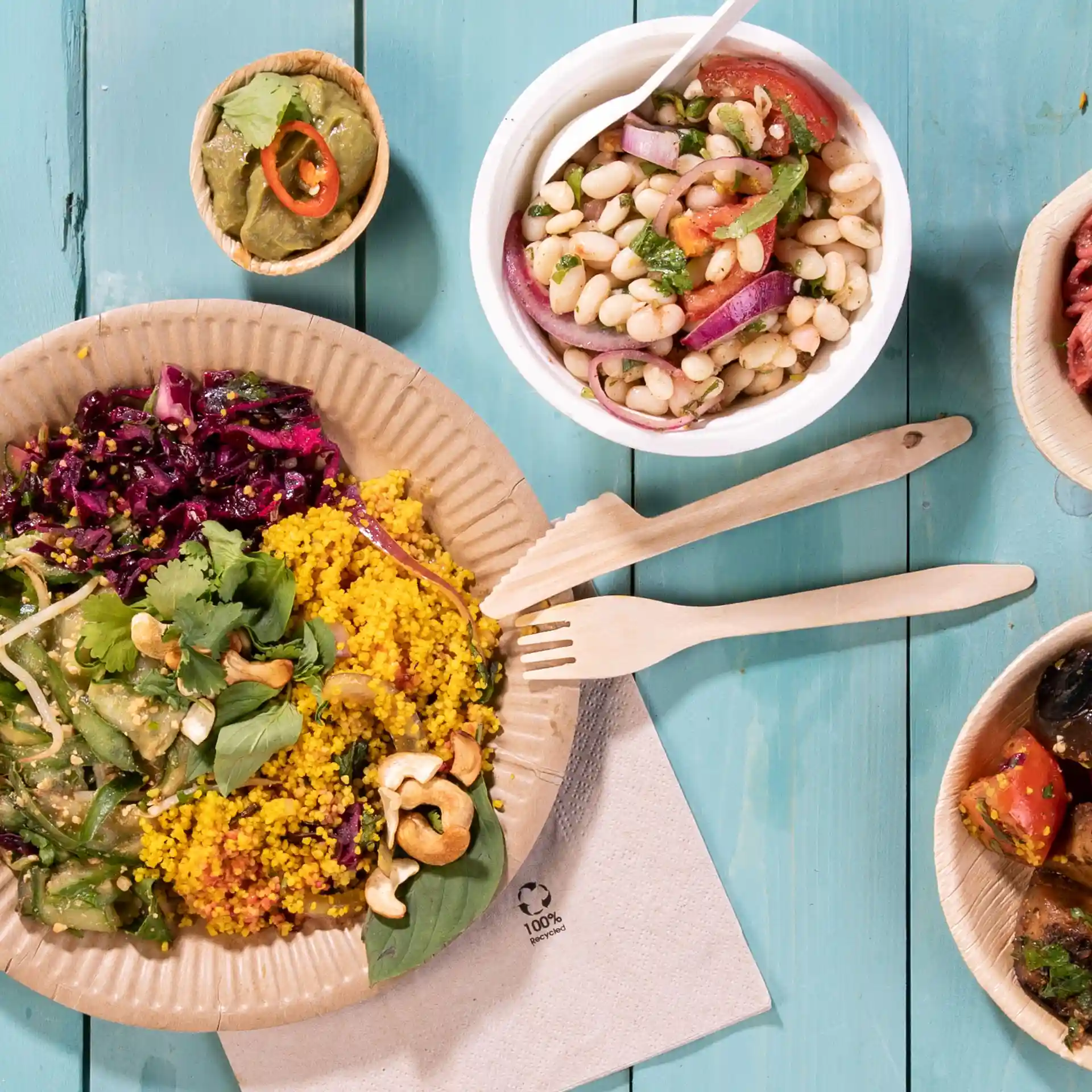 Image of a plate with colorful food including couscous, salad, and garnishes, accompanied by wooden forks and small bowls of toppings.