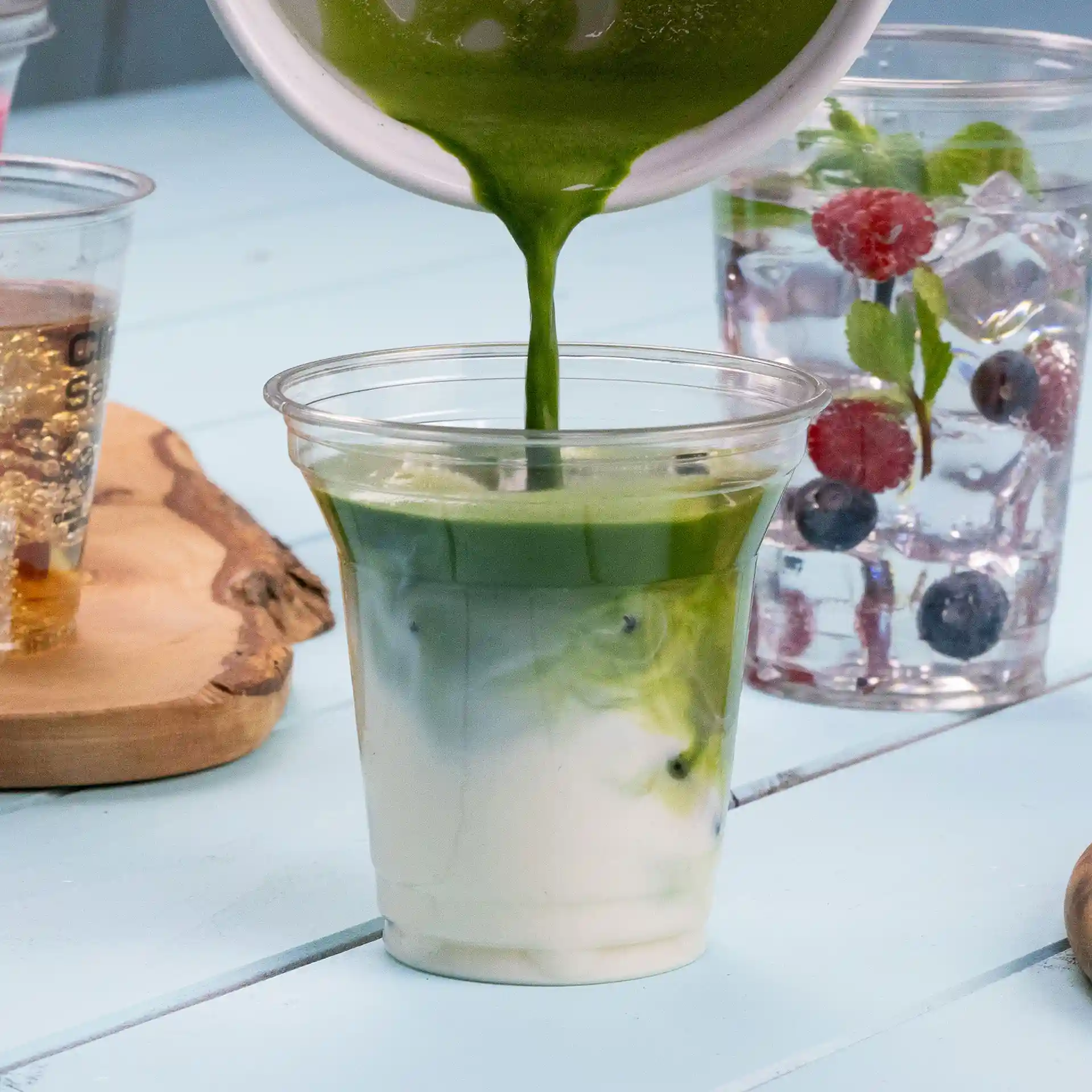Clear rPET cup filled with layered green and white beverage, placed on a light blue surface.