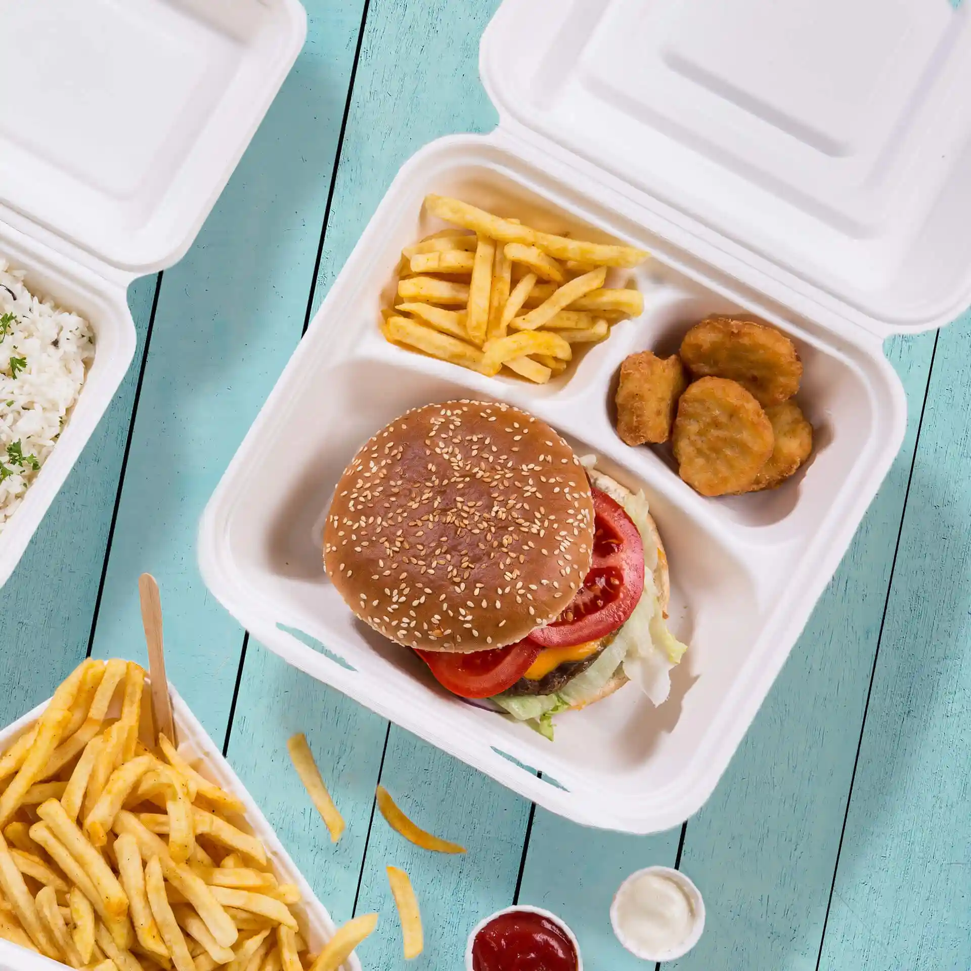 Image of a white sugarcane container with three compartments, featuring a burger, fries, and chicken nuggets.