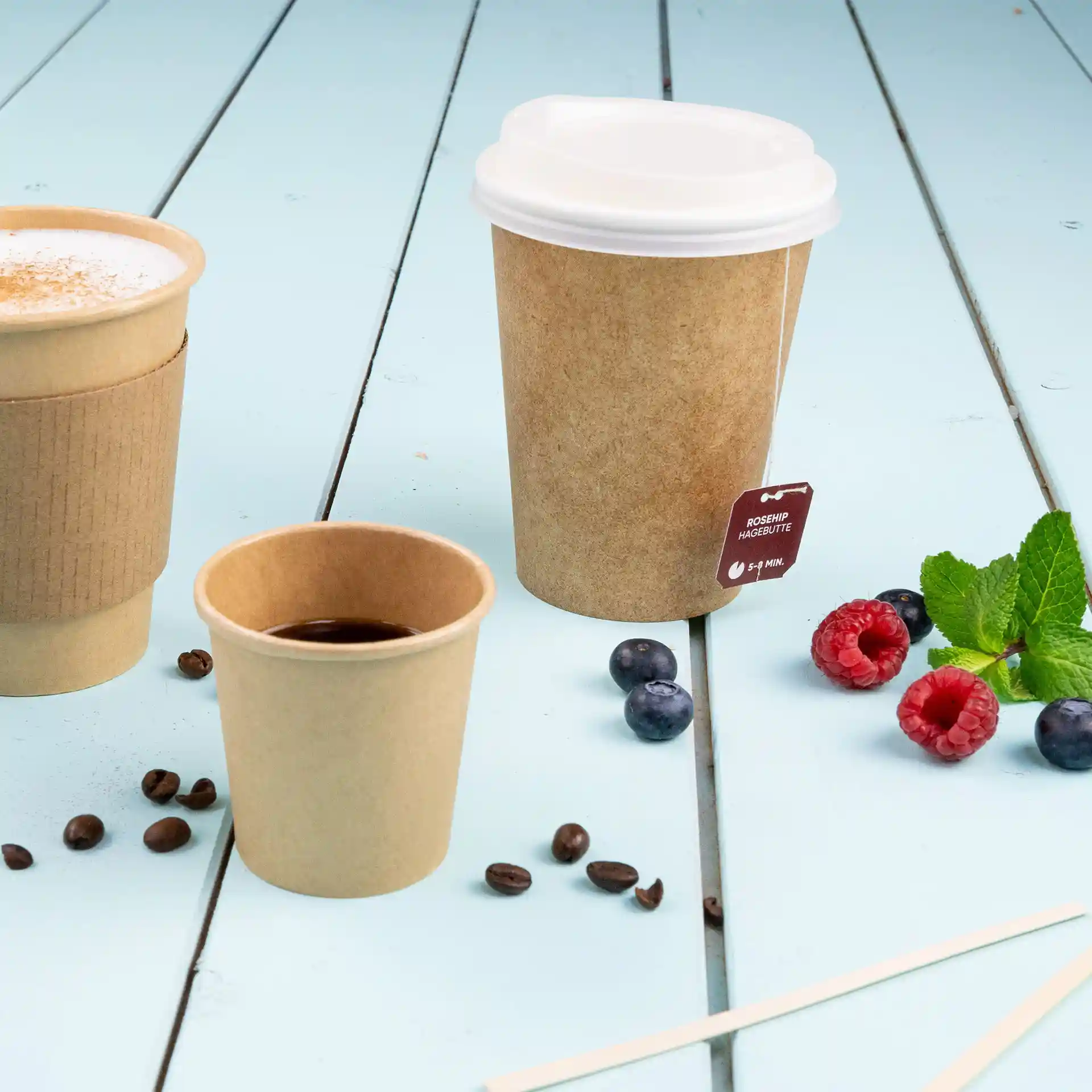 Image of three paper cups on a blue wooden surface; one is a 100 ml brown cup with a white lid, another is a smaller brown cup, and a third is filled with coffee.
