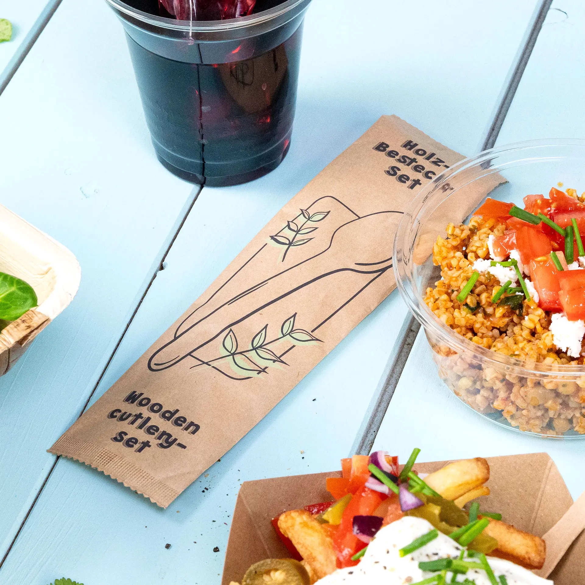 Holzbesteckset mit Löffel und Serviette präsentiert; enthält einen biologisch abbaubaren Beutel und ist für warme oder kalte Speisen geeignet.