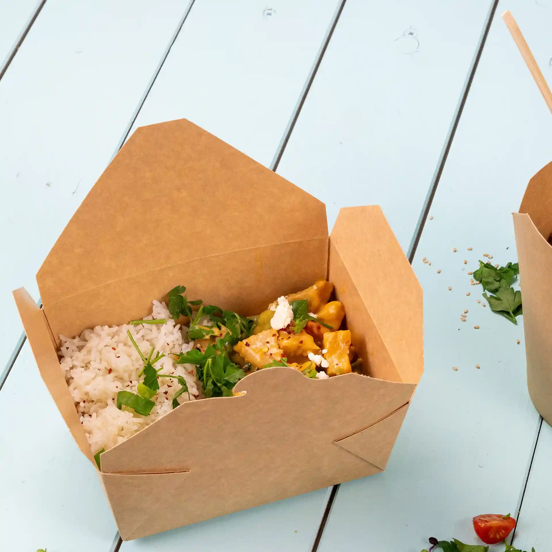 Brown takeaway container filled with rice and vegetables, placed on a light blue surface.