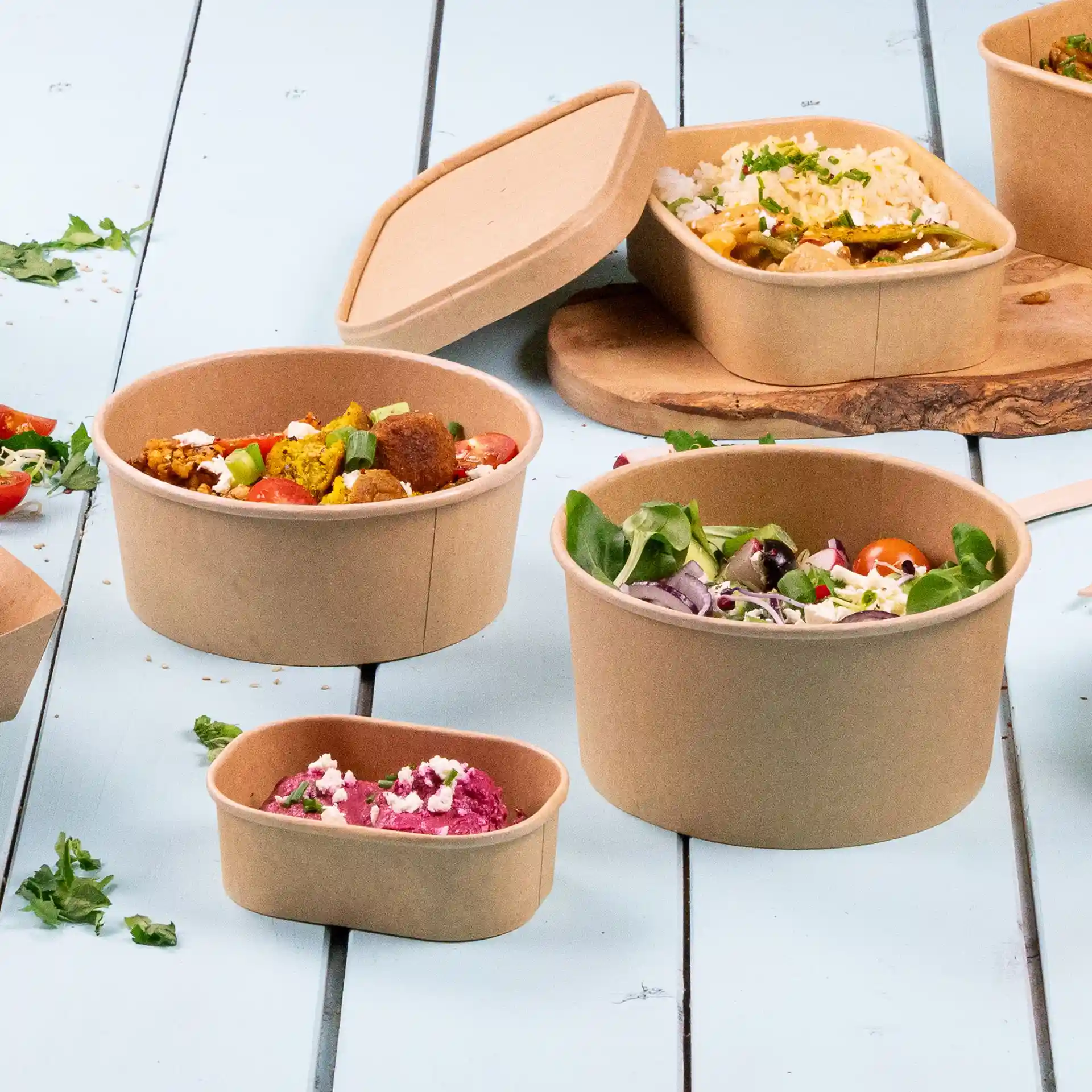Round brown paper bowls with eco-friendly coating, varying sizes, filled with food items on a light blue surface.