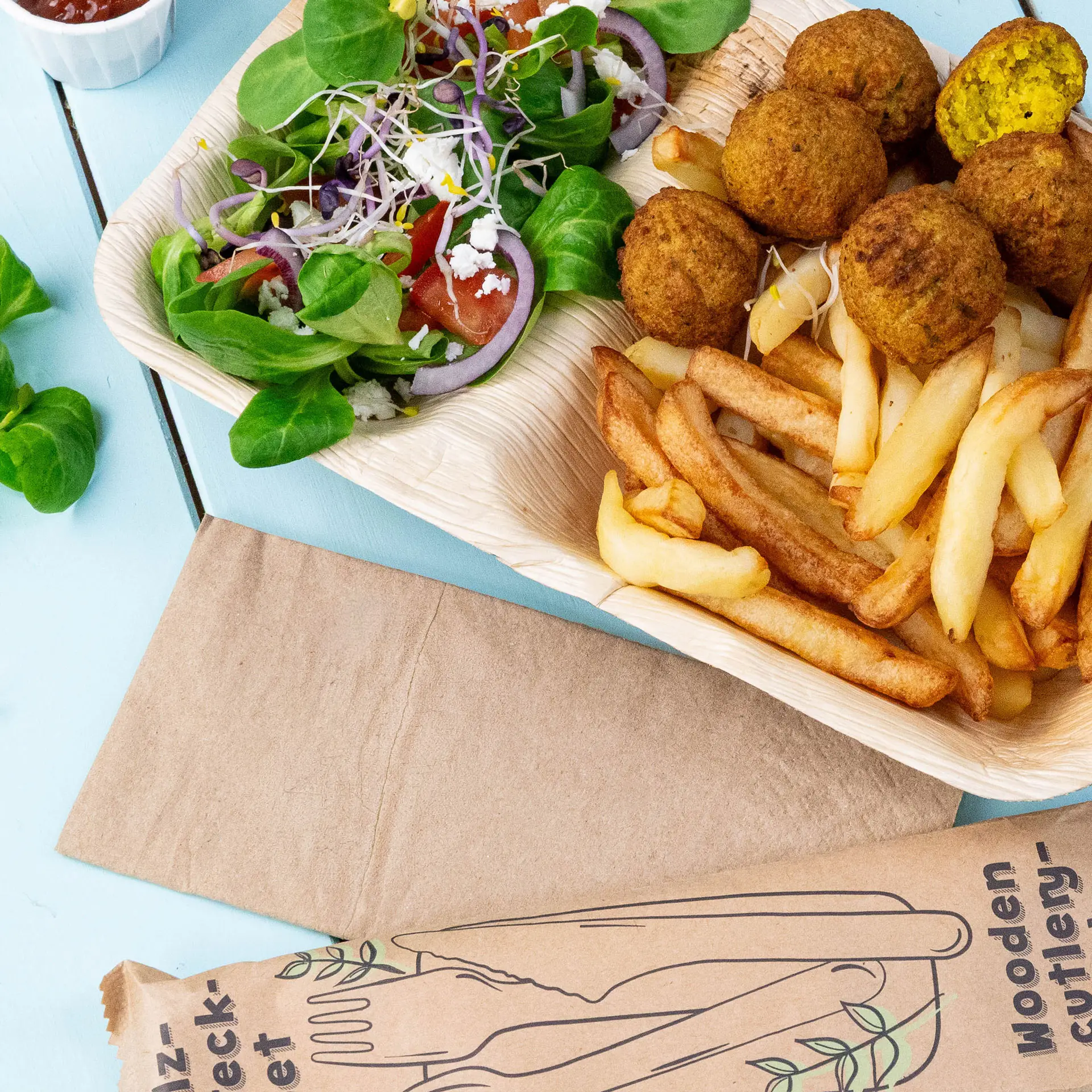 Bild eines Holztabletts mit Falafelbällchen, Pommes frites und einem gemischten Salat mit Blattgemüse, Tomaten und Zwiebeln.
