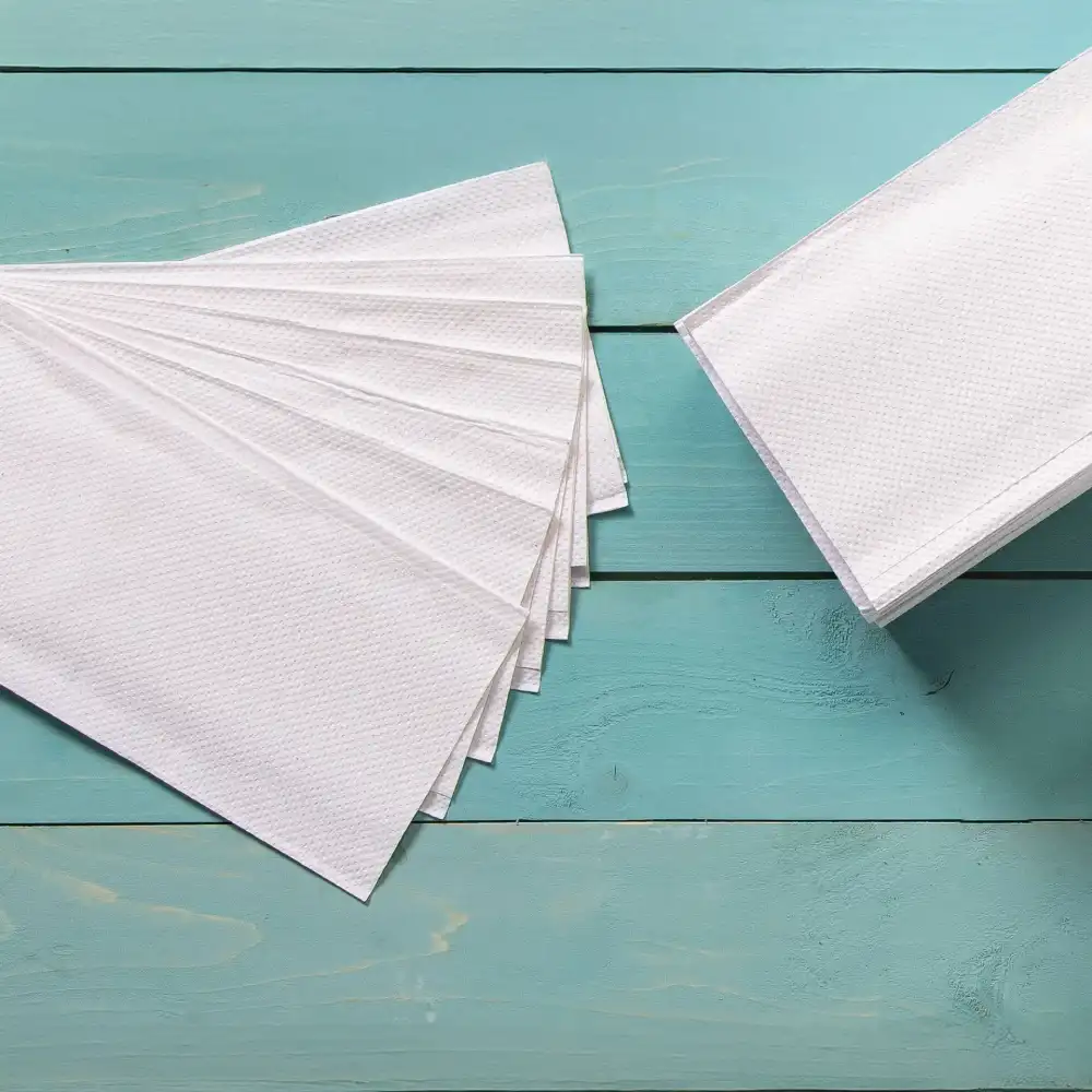 White tissue papers arranged in a fan shape with additional folded tissue paper nearby on a light blue wooden surface.