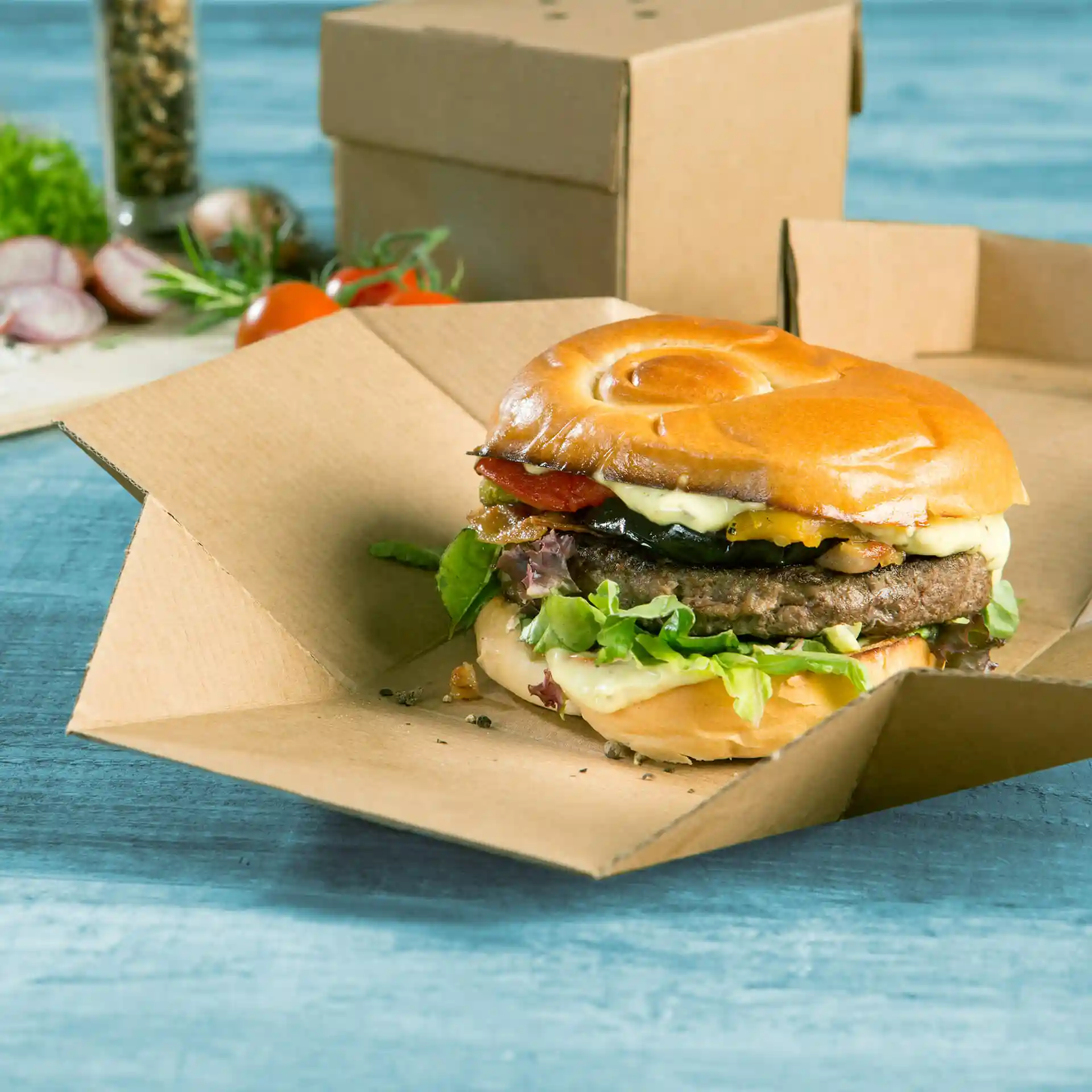 Burger in einer faltbaren braunen Pappschachtel, mit Salat, Käse, Speck und einem weichen Brötchen.