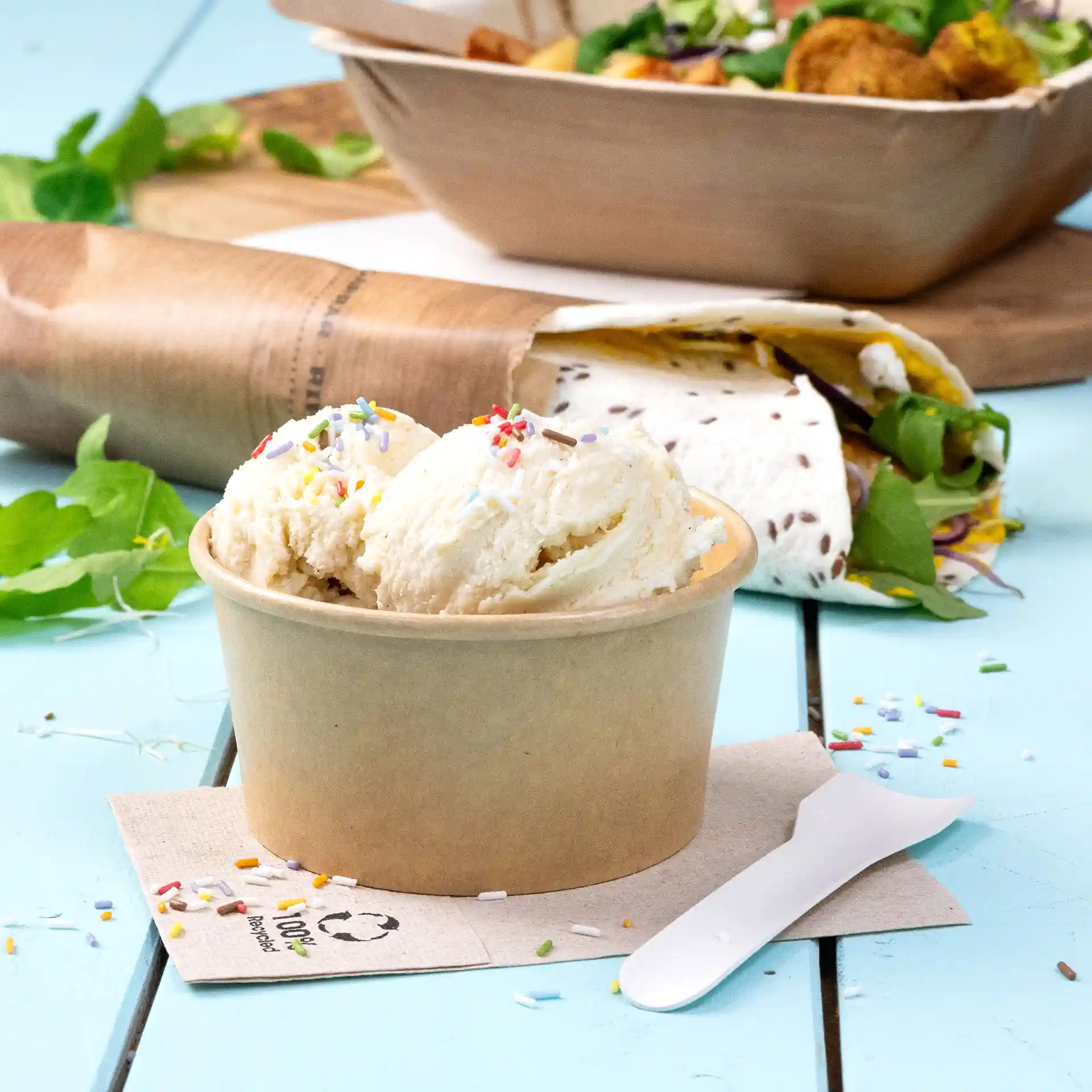 Brauner Becher mit Eiscreme und bunten Streuseln, dazu ein weißer Löffel und eine Serviette.